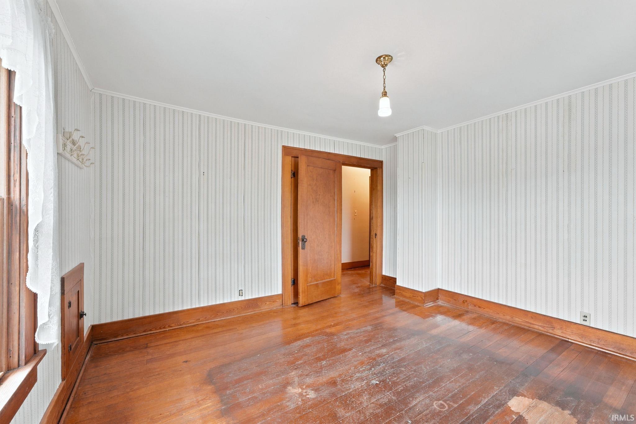 Interior room featuring wood-finish flooring, striped wall covering, and a brass-finished pendant light fixture