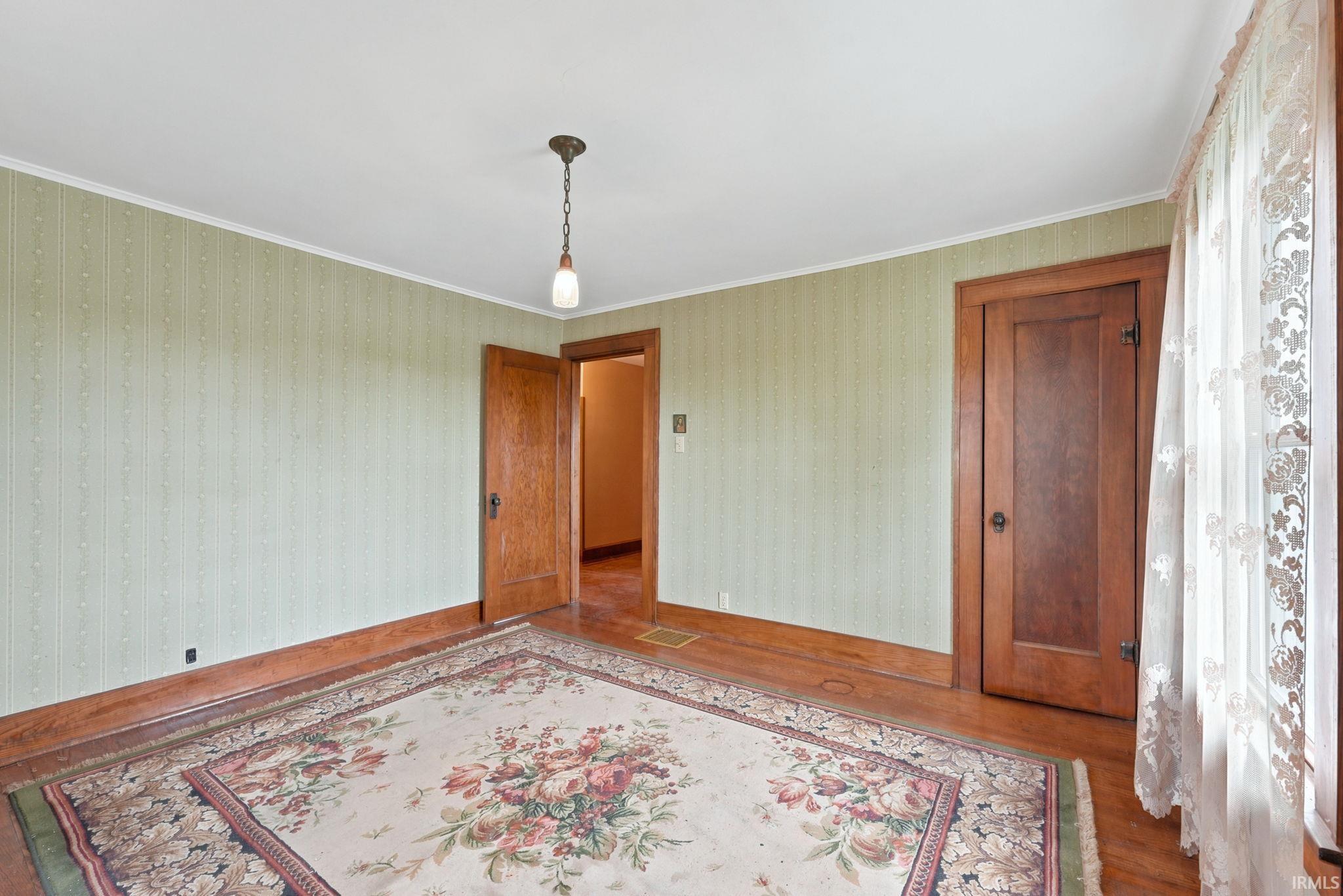 Room featuring light green patterned wallpaper, wood-finish flooring, and a single pane window with sheer white lace curtains