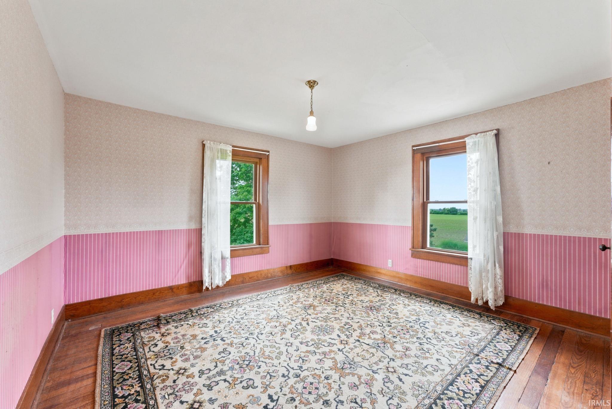 Spacious room featuring hardwood flooring, two large windows, a ceiling light fixture, and textured wallpaper