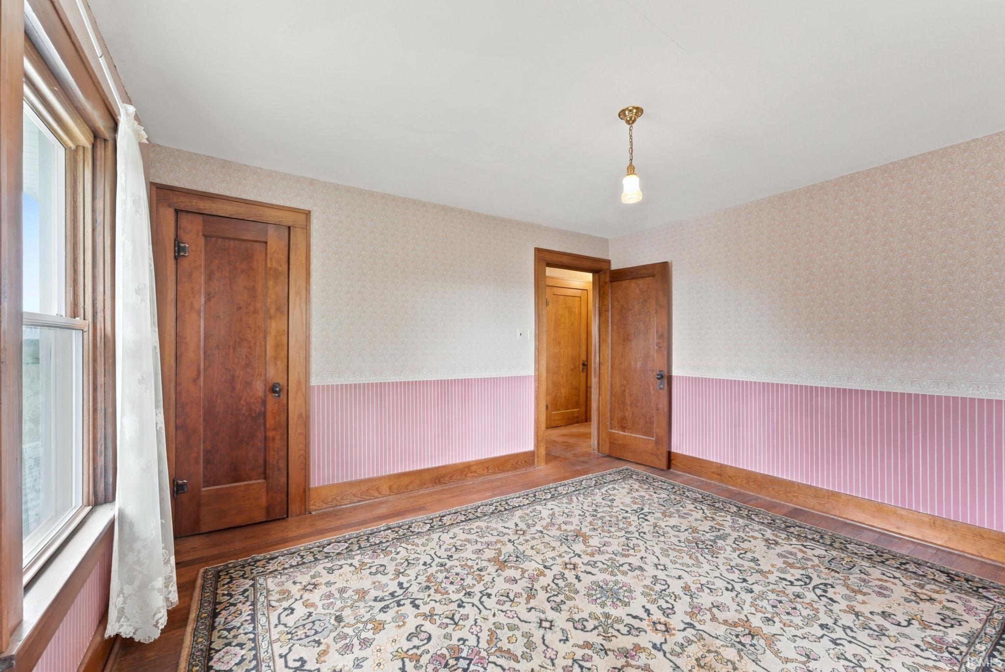 Interior room with wood-finish flooring, two solid wood panel doors, a window with wood trim, and a ceiling-mounted light fixture