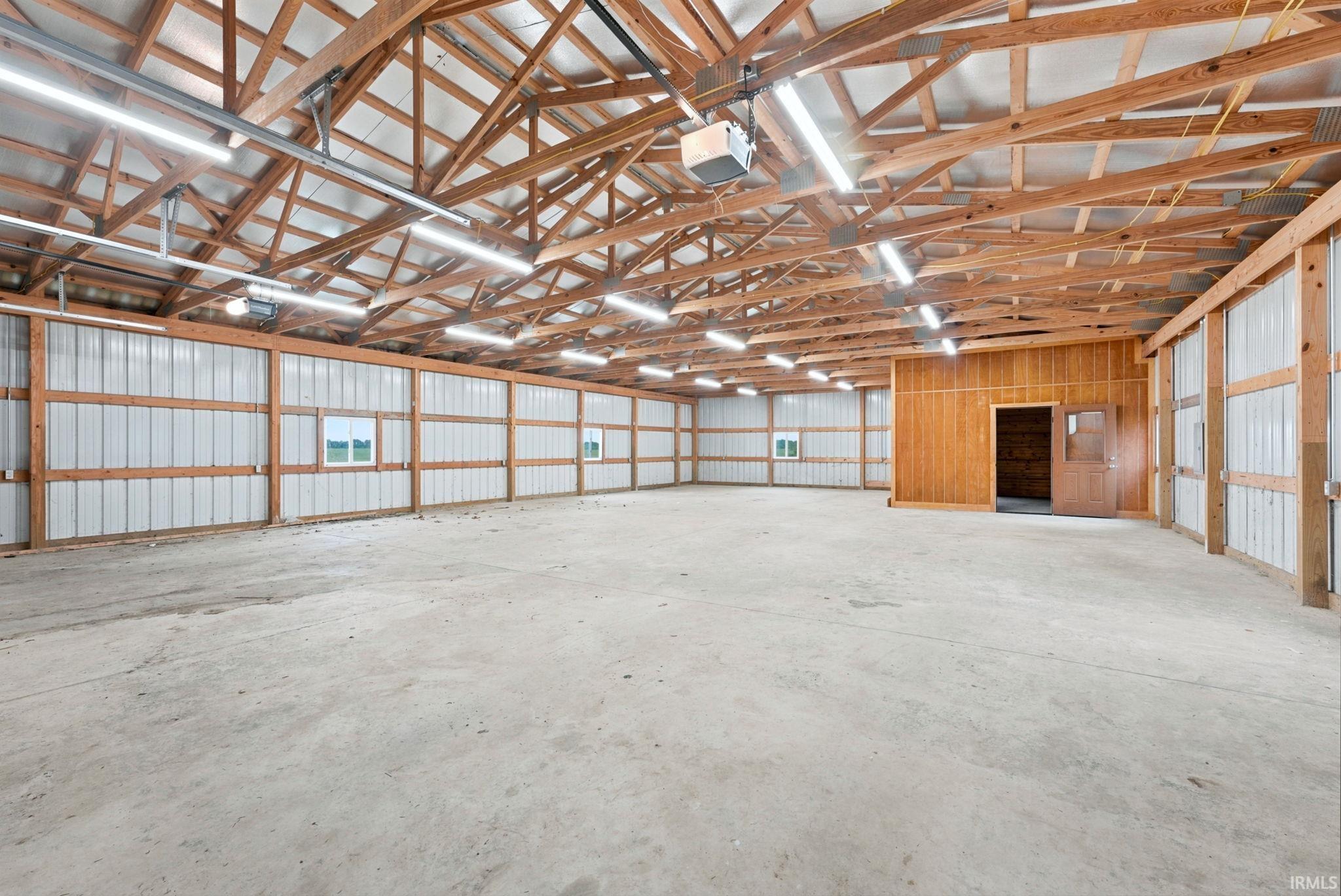 Spacious interior with exposed wooden truss ceiling, concrete flooring, and ample overhead lighting