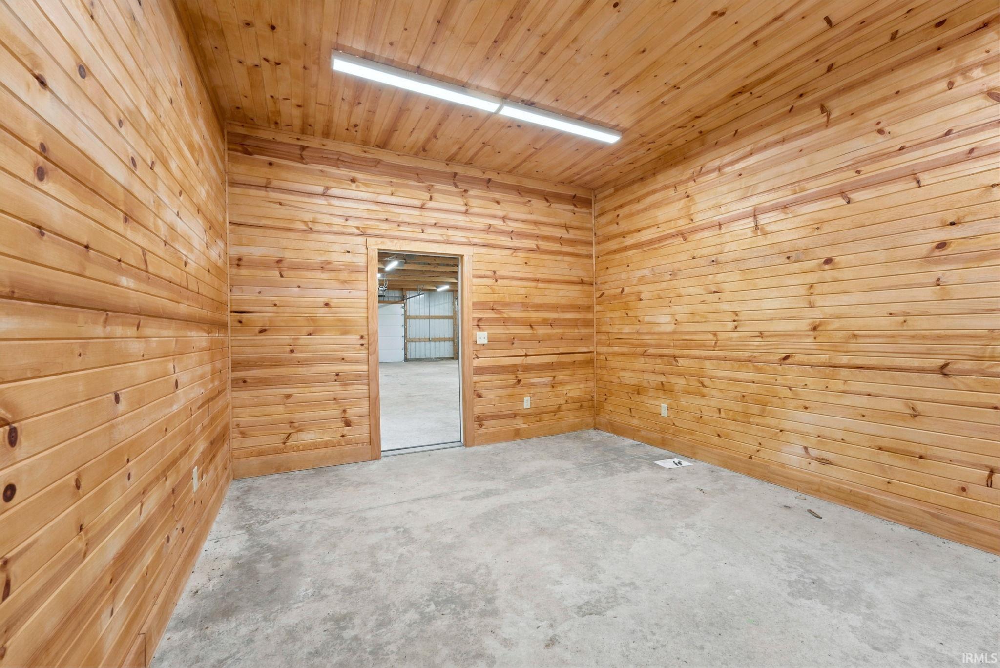 Interior room featuring tongue and groove wood paneling on walls and ceiling, concrete flooring, and an open doorway
