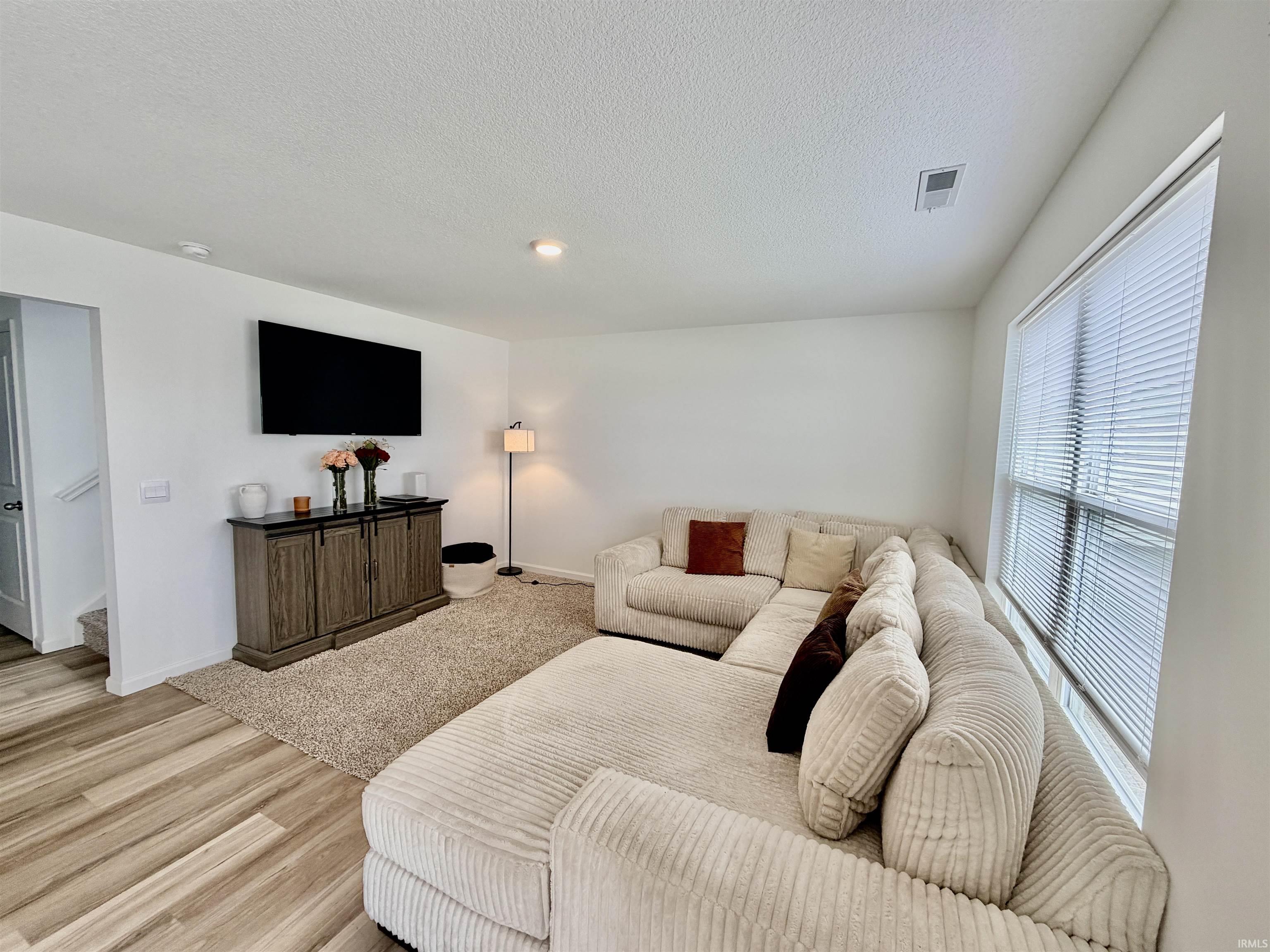 Bright living area featuring wood-finish flooring, white walls, and a large window with blinds