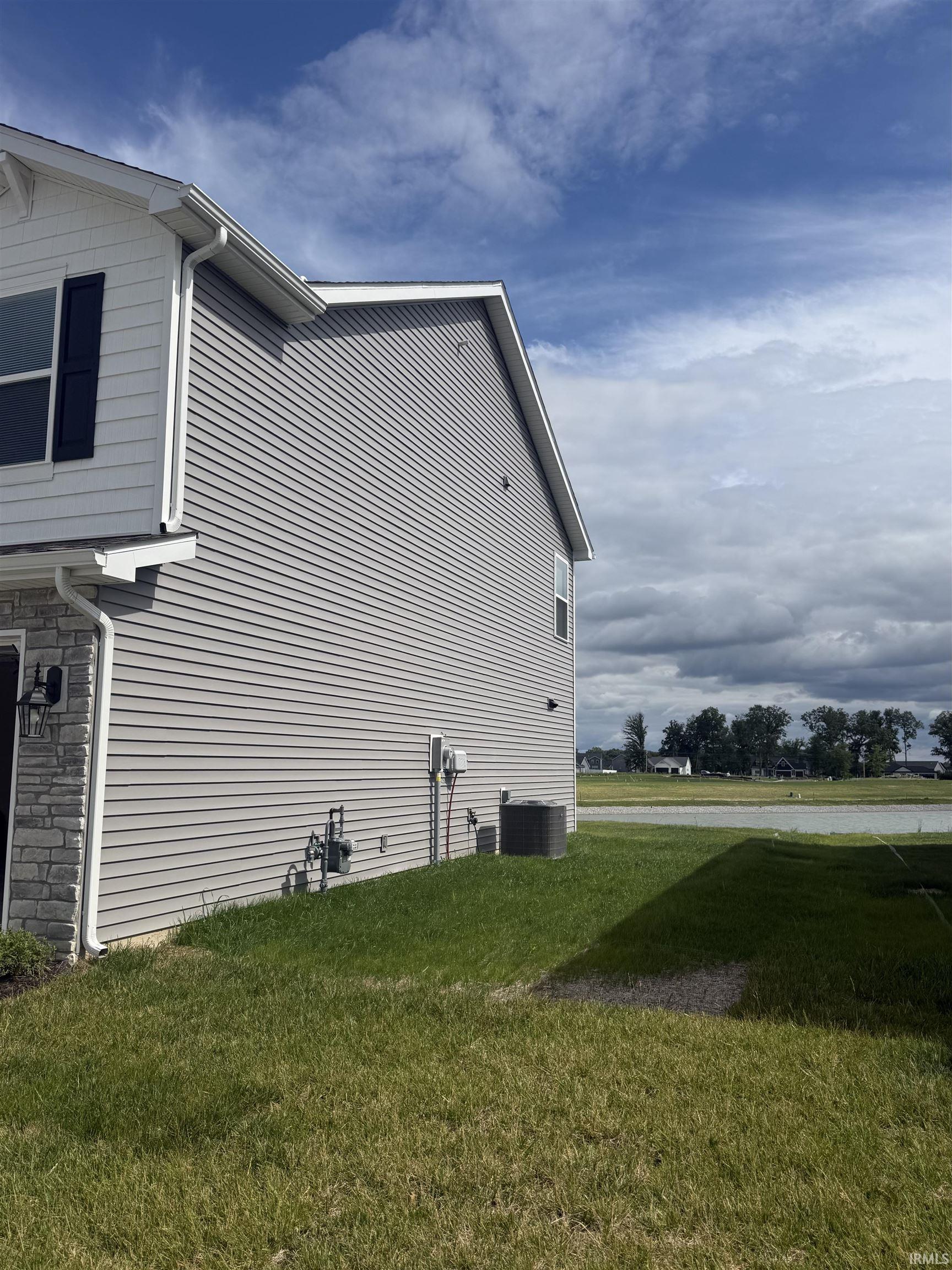 Side exterior featuring gray horizontal siding, white trim, and a stone accent column