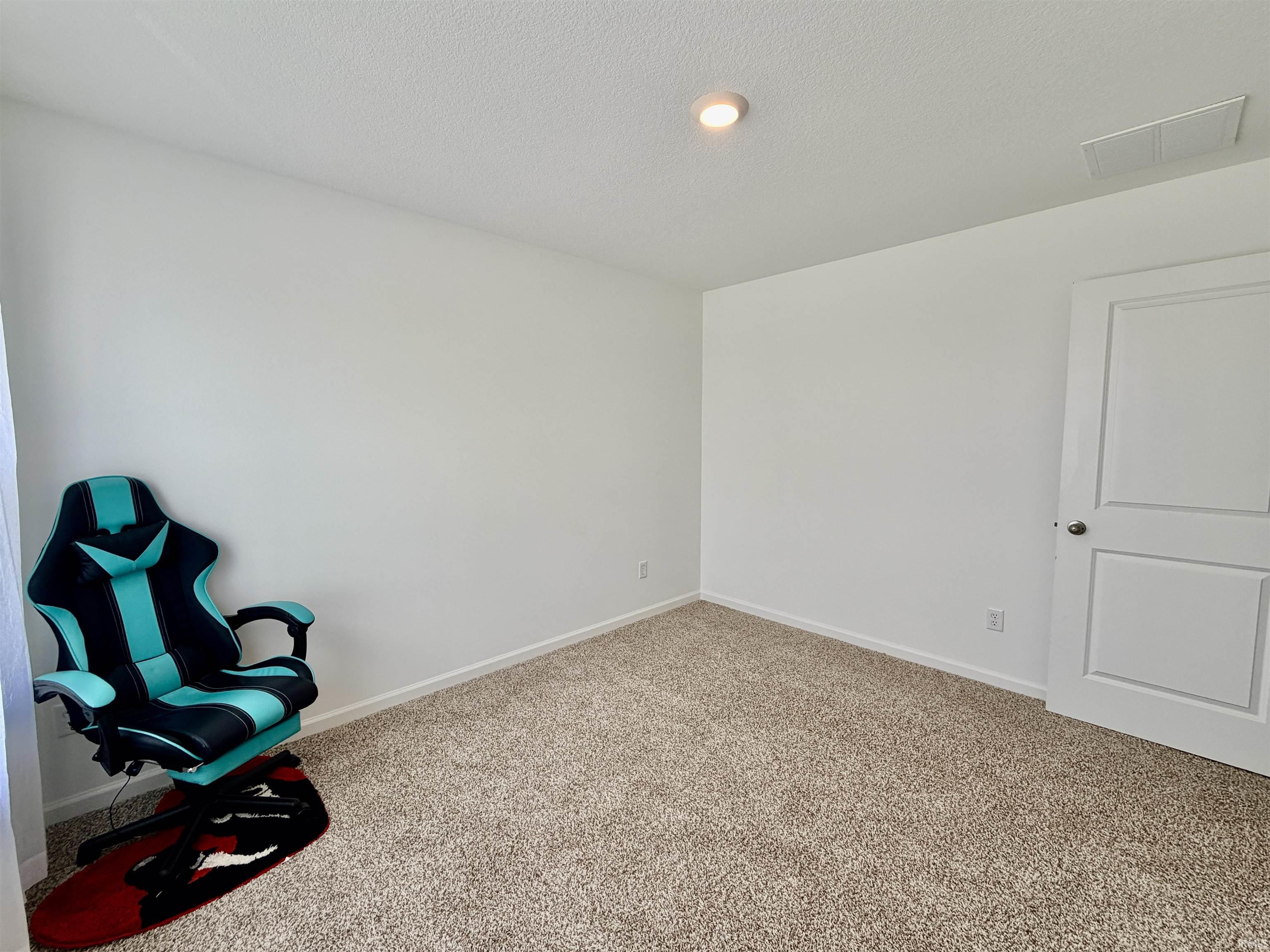 Carpeted room featuring neutral wall paint, a white paneled door with a silver knob, and a ceiling-mounted light fixture
