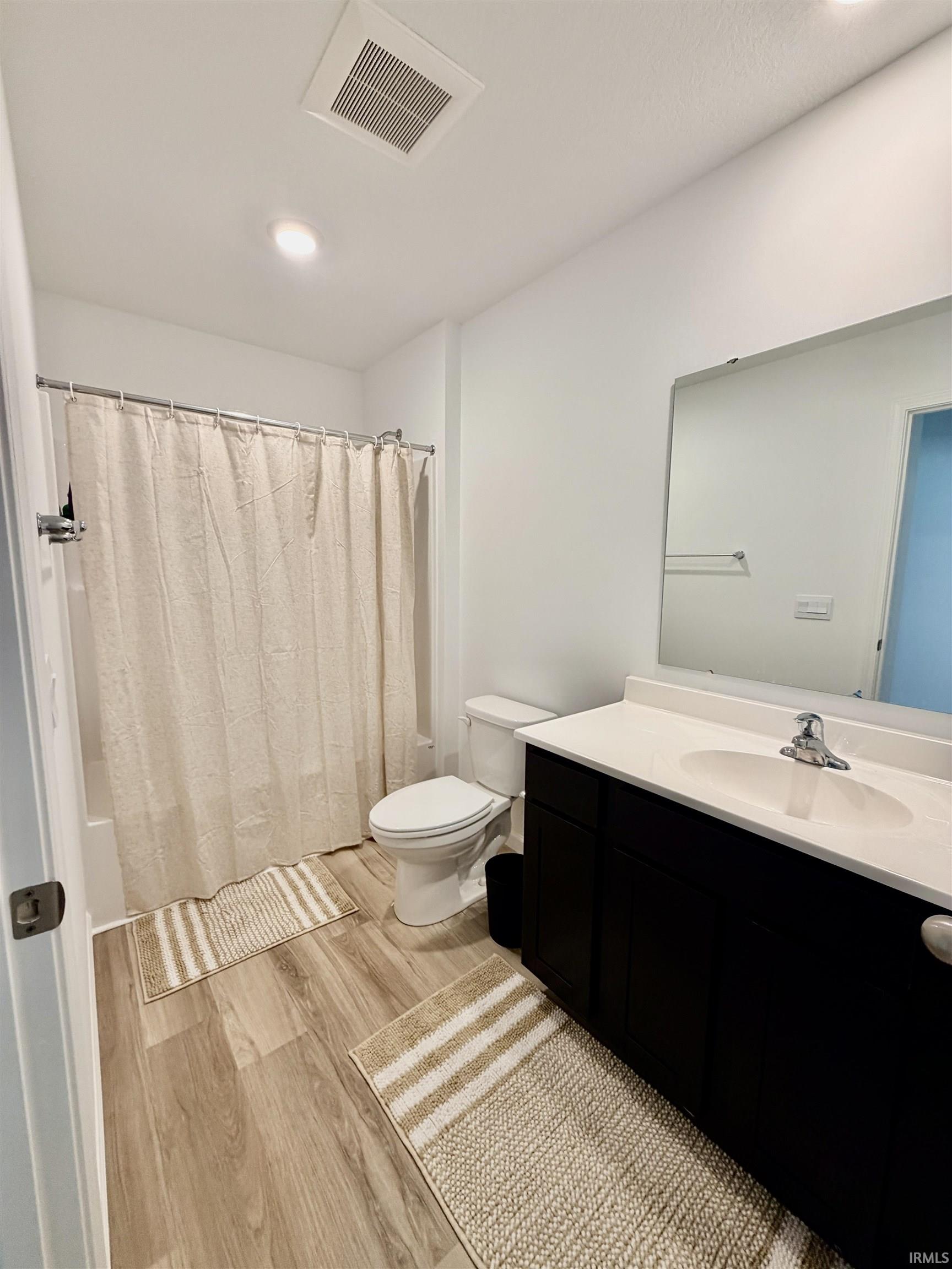 Bathroom with wood-finish flooring, a dark wood-finish vanity, a white countertop, and a shower-tub combination