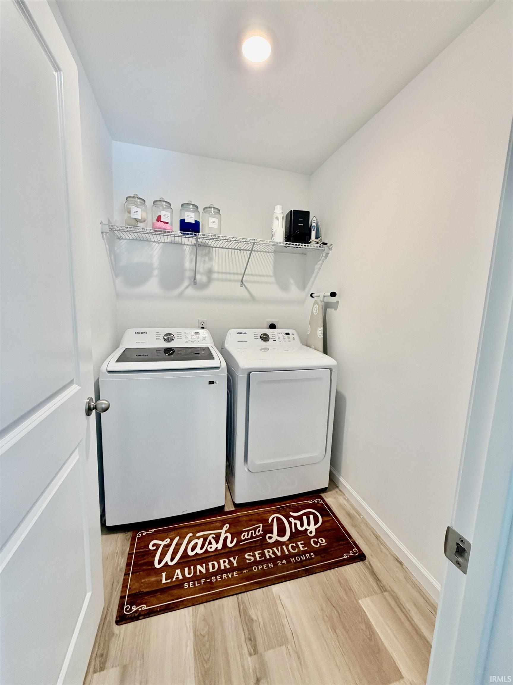 Dedicated laundry area featuring a washer and dryer, wood-finish flooring, a wall-mounted wire shelf, and a ceiling light fixture