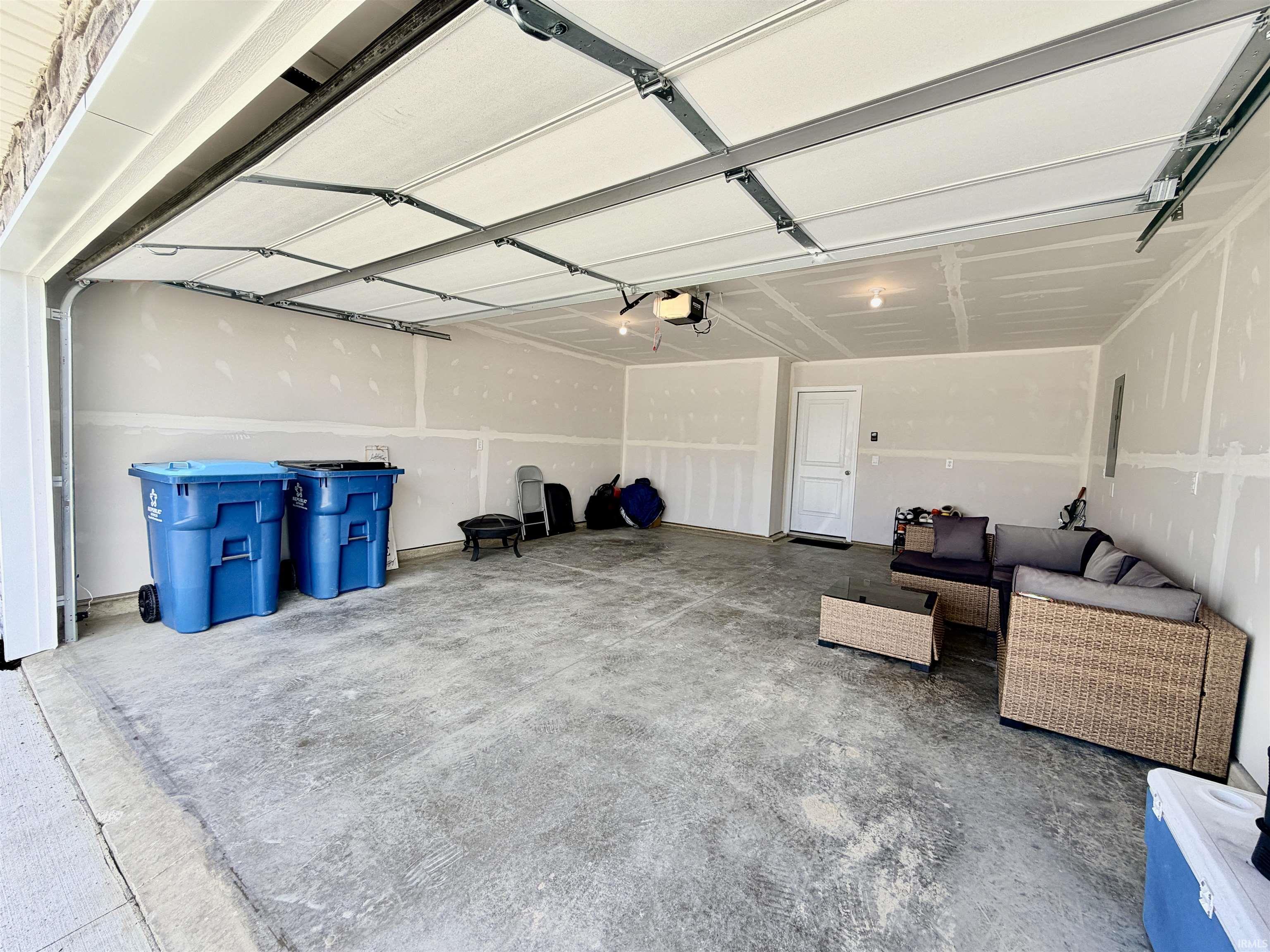 Spacious garage with a textured concrete floor, exposed drywall, and a white overhead garage door