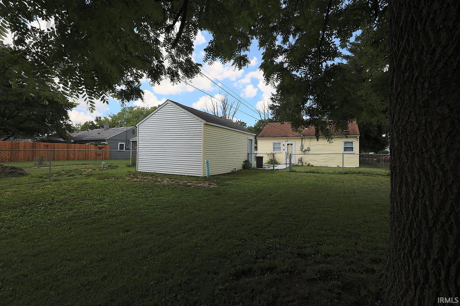 Expansive backyard featuring a detached garage with white siding, a single-story residence with yellow siding and a red shingle roof, and a combination of chain-link and wood fencing