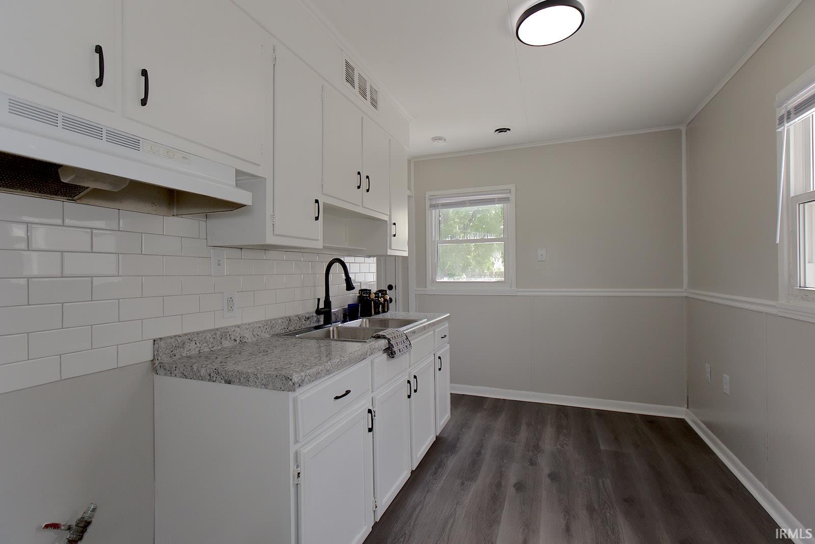 Modern kitchen featuring white cabinetry, black hardware, wood-finish flooring, a contemporary black faucet, and a subway tile backsplash