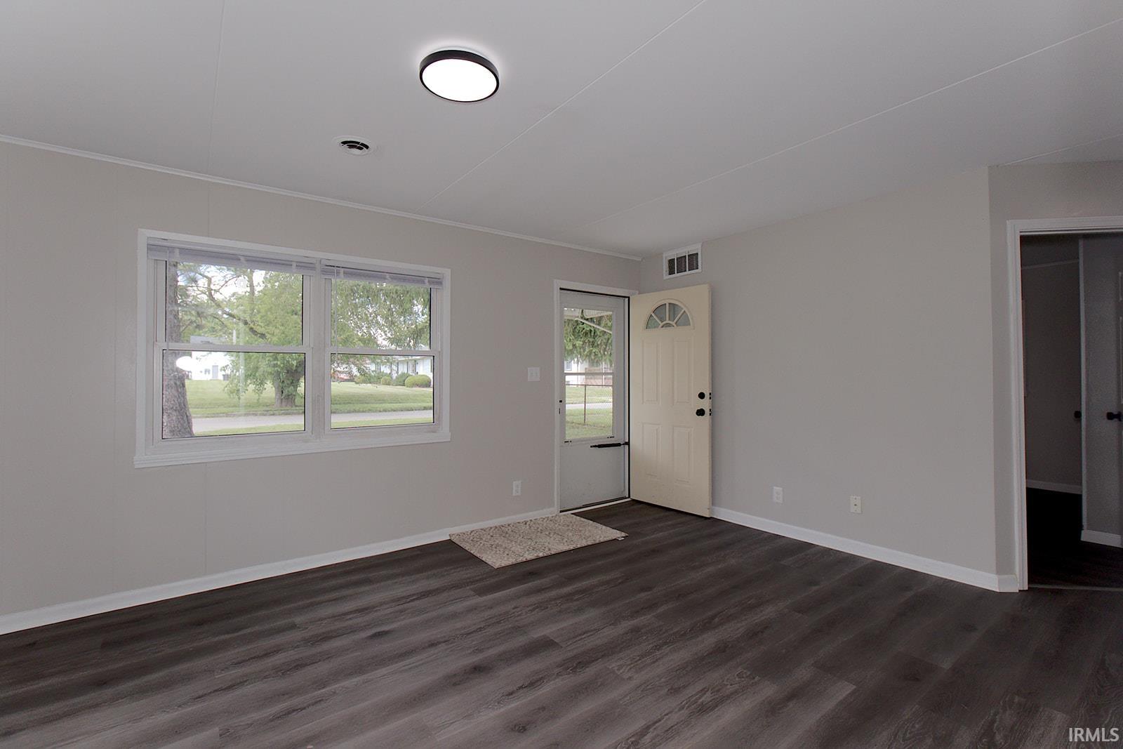 Spacious room featuring dark wood-finish flooring, light gray wall paint, and white trim