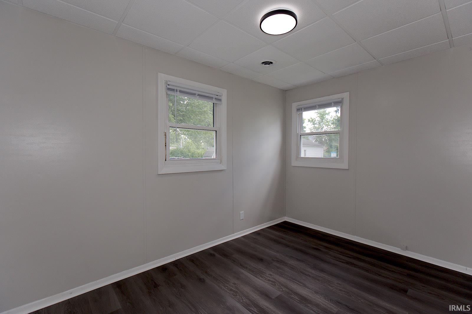 Room featuring wood-finish flooring, two windows with white trim, and light gray wall panels