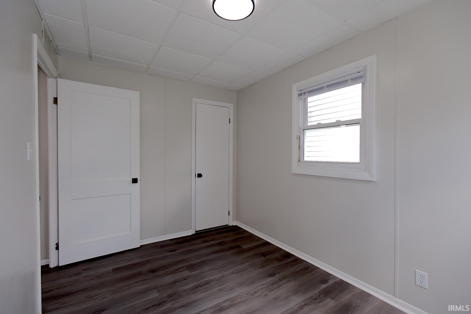 Interior room featuring wood-finish flooring, light gray walls, a window with horizontal blinds, and a white flush-mount ceiling light