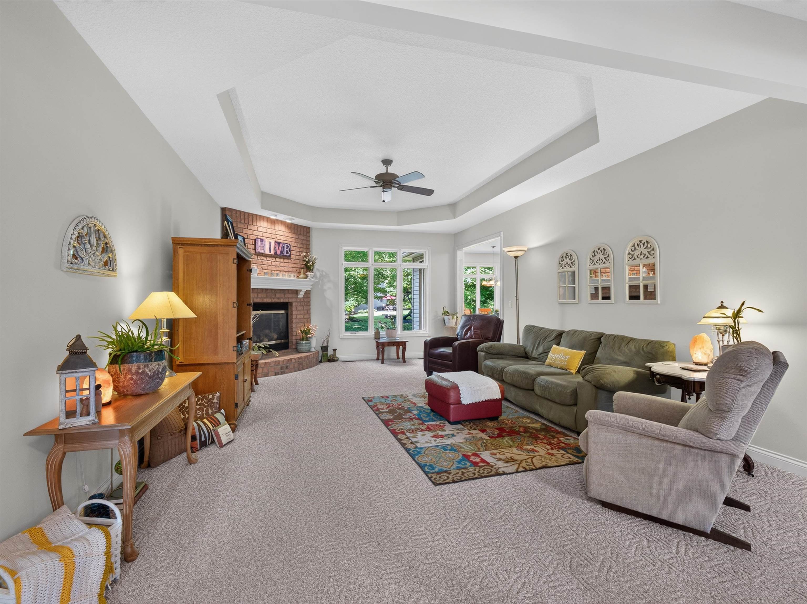 Living room featuring a tray ceiling, corner brick fireplace with a white mantel, and light-colored patterned carpeting
