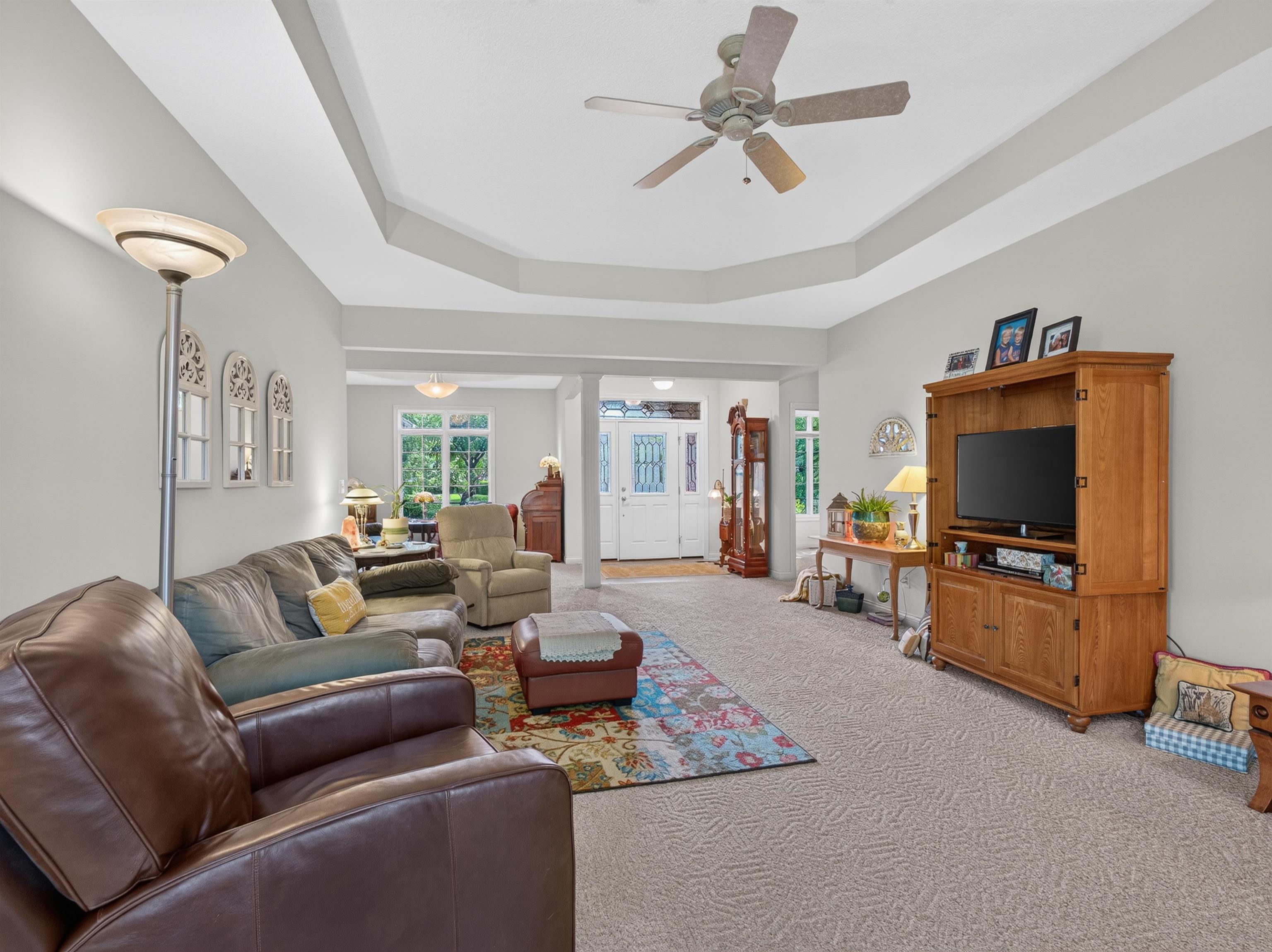 Spacious living area featuring a tray ceiling with a ceiling fan, light-toned carpeting, and an open layout connecting to additional rooms