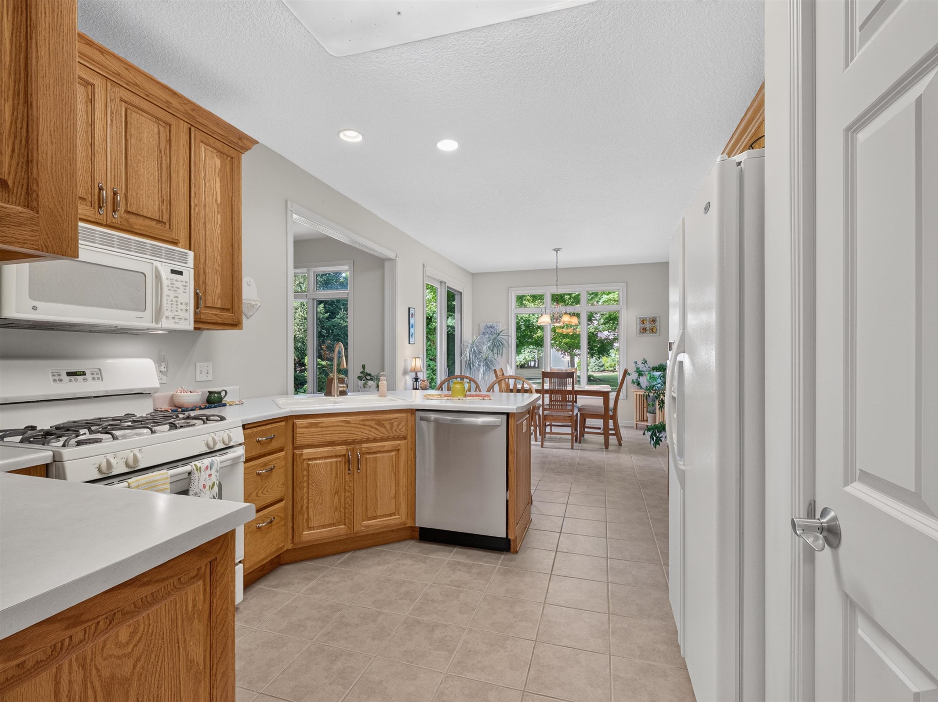 Spacious kitchen featuring light wood cabinetry, light countertops, white appliances, and tiled flooring