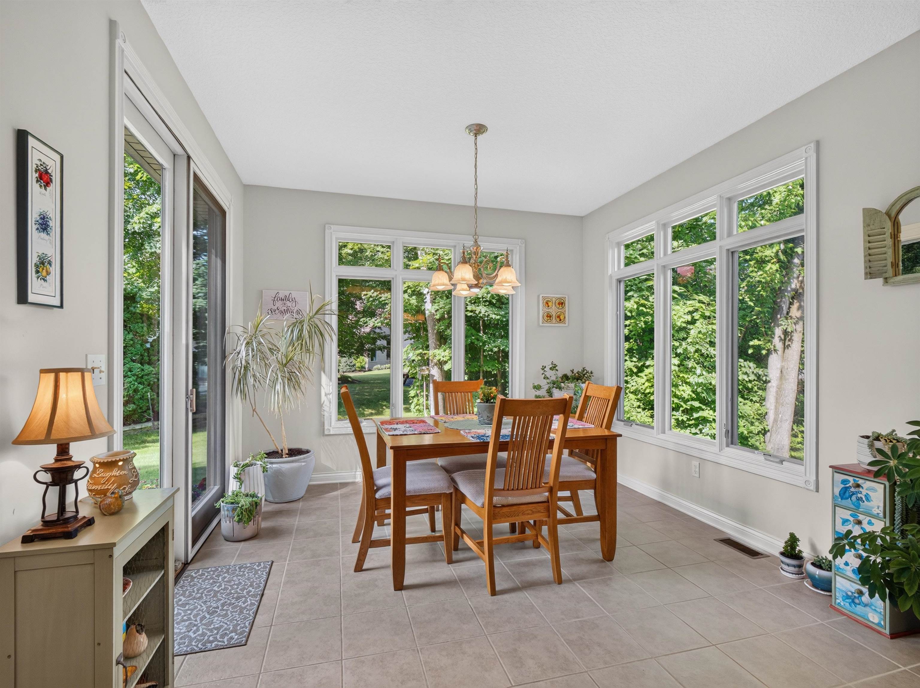 Light-filled dining area featuring expansive windows, ceramic tile flooring, a glass-paneled exterior door, and a ceiling-mounted chandelier