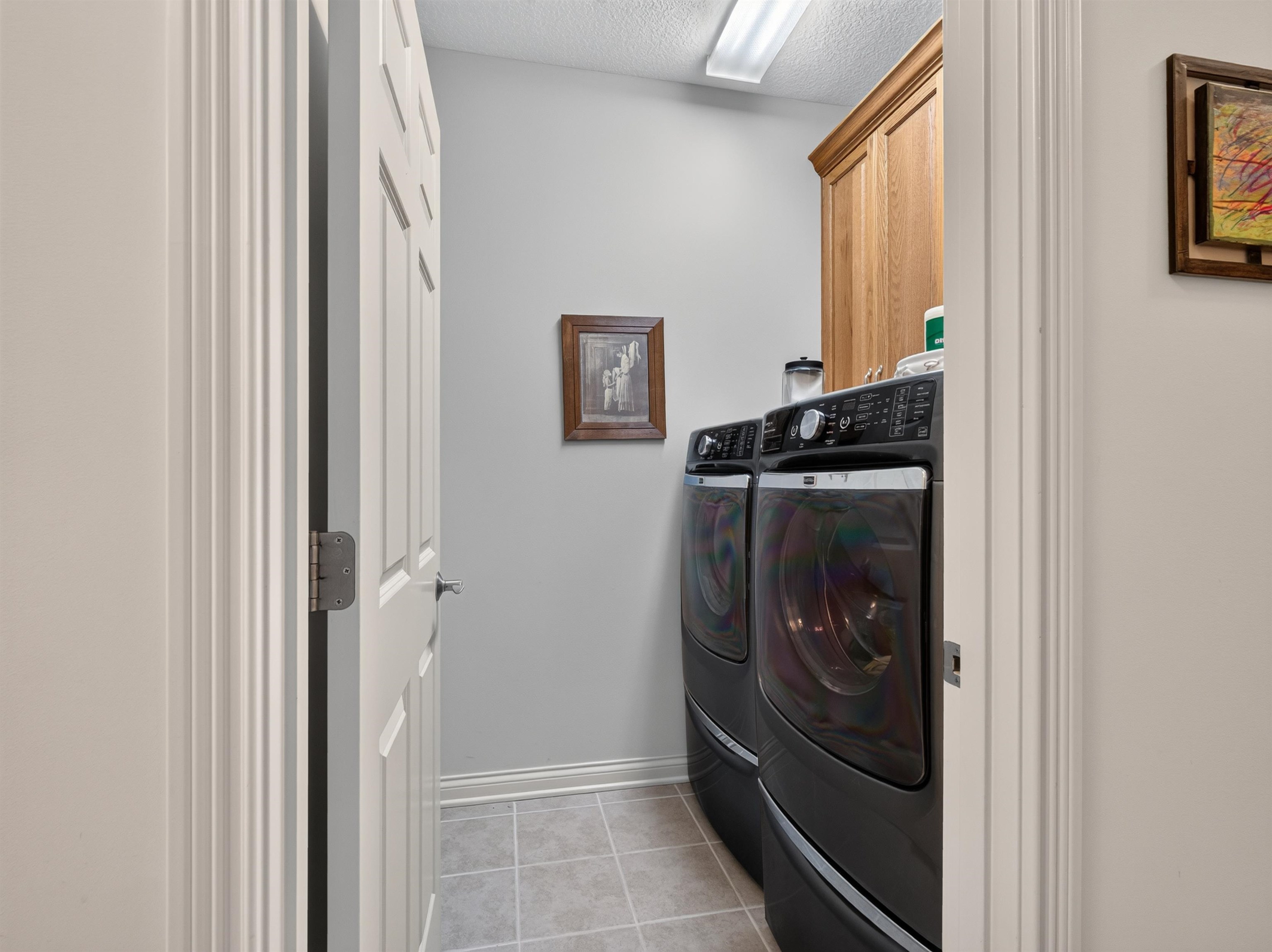 Dedicated utility space featuring light gray walls, light gray tile flooring, and a built-in wooden storage cabinet
