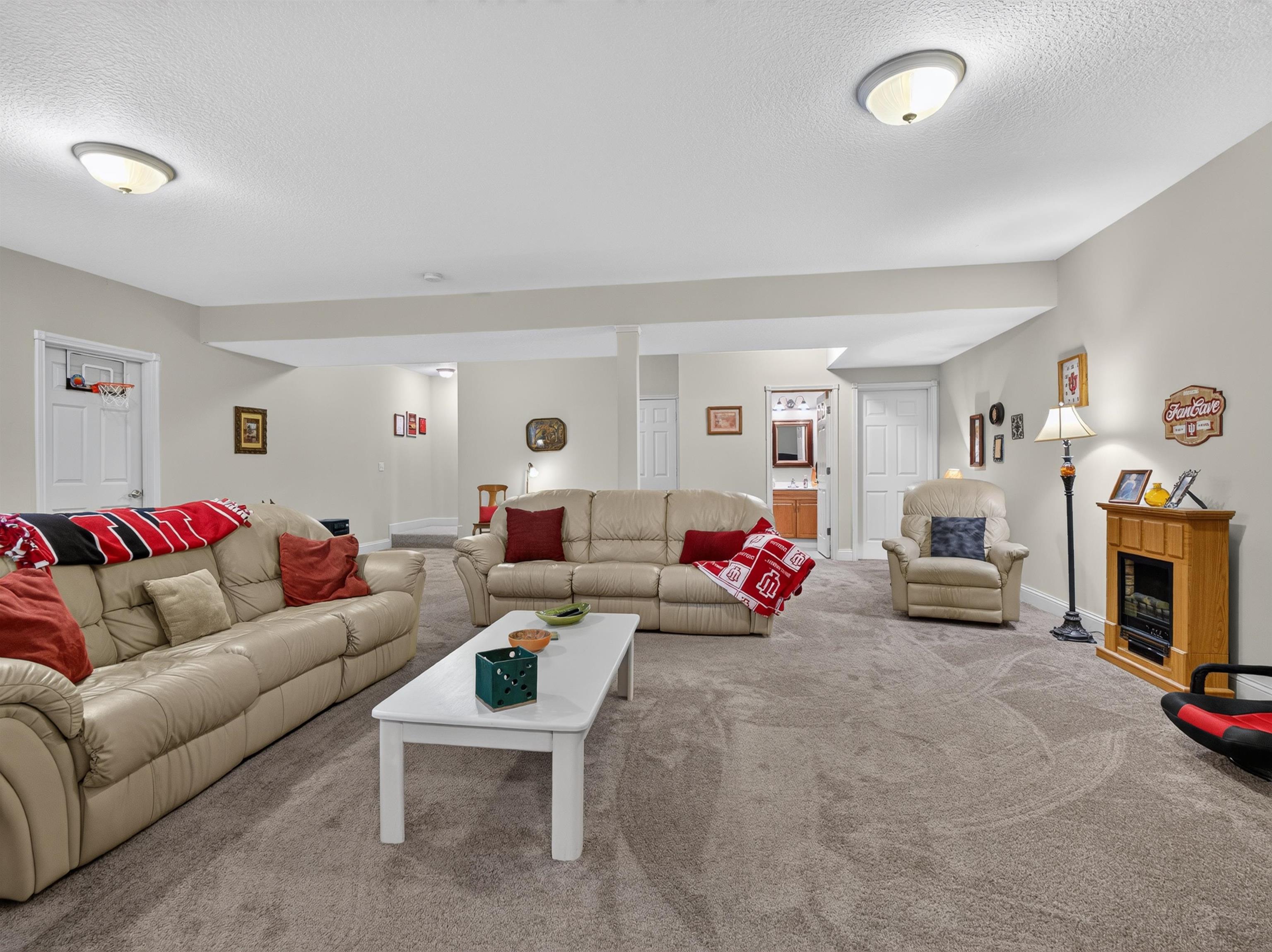 Carpeted living area featuring recessed ceiling lights, neutral wall tones, and a visible doorway to an additional room with a vanity