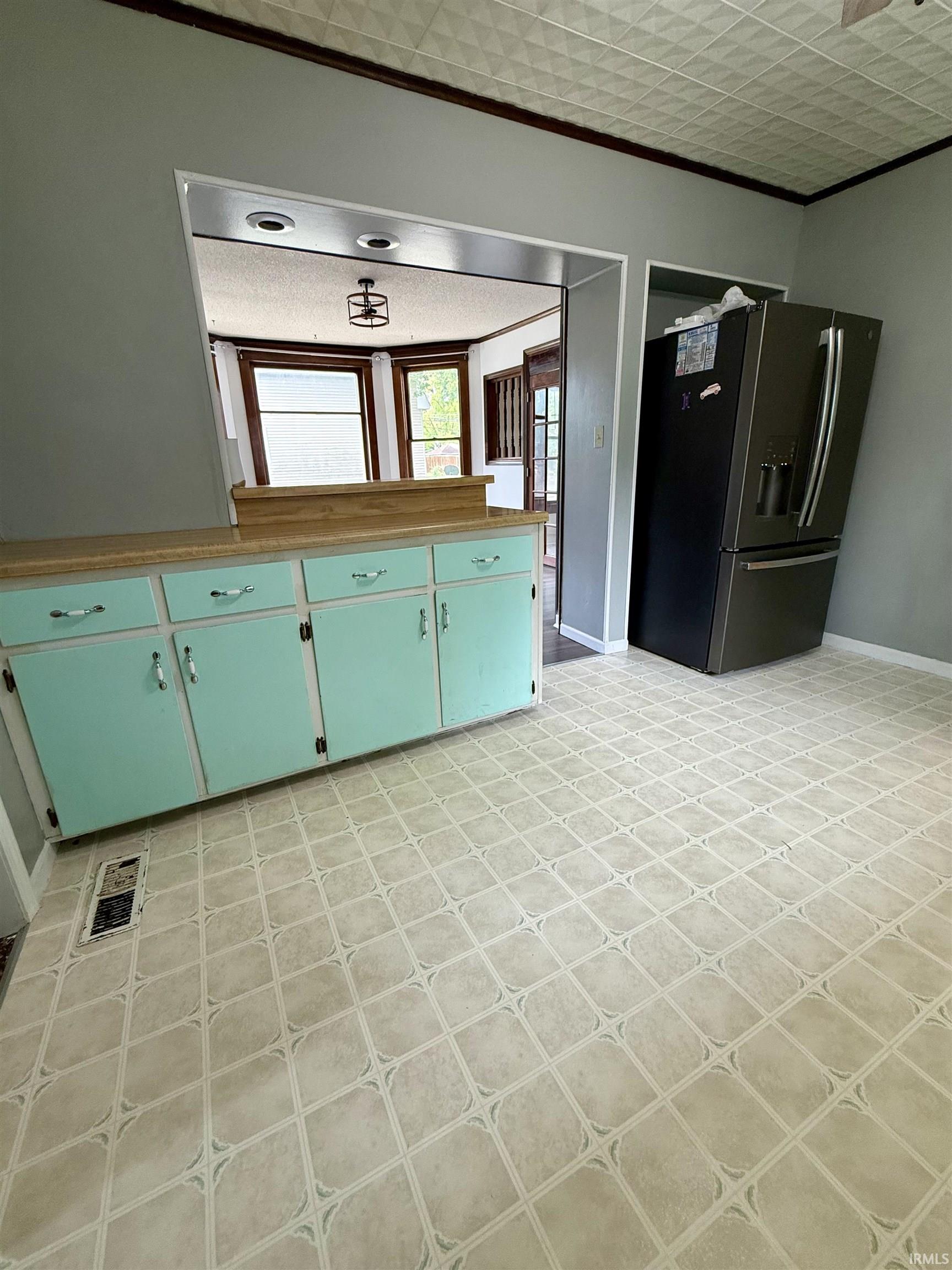 Kitchen area featuring patterned vinyl flooring, a mint green base cabinet with a light-colored countertop, and a built-in pass-through window to an adjacent room