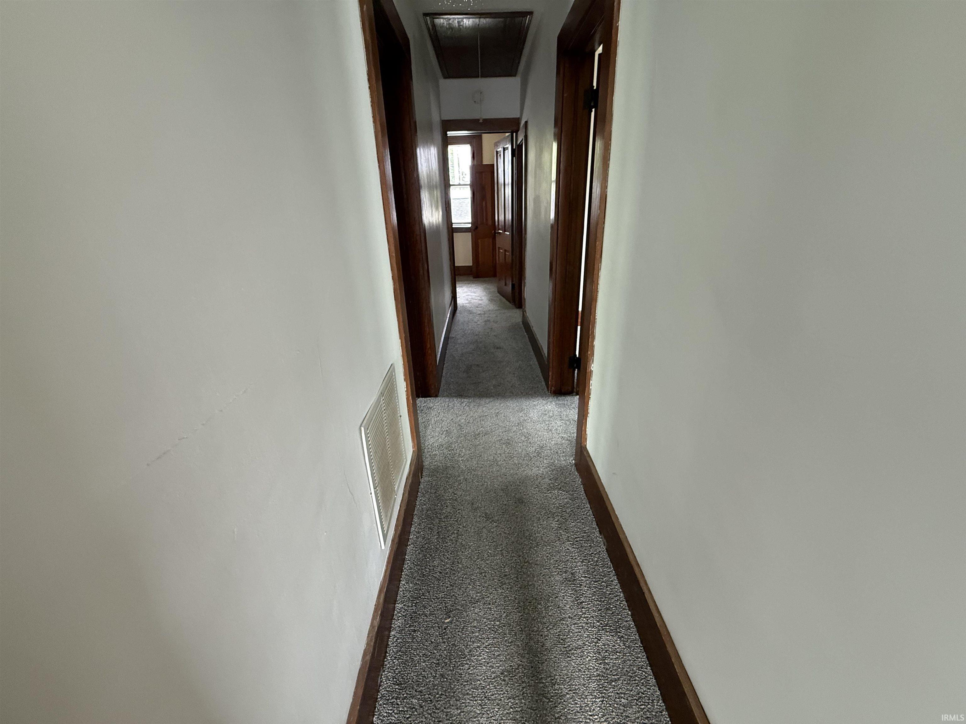Hallway featuring light gray carpet flooring, white painted walls, and dark wood trim around doorways