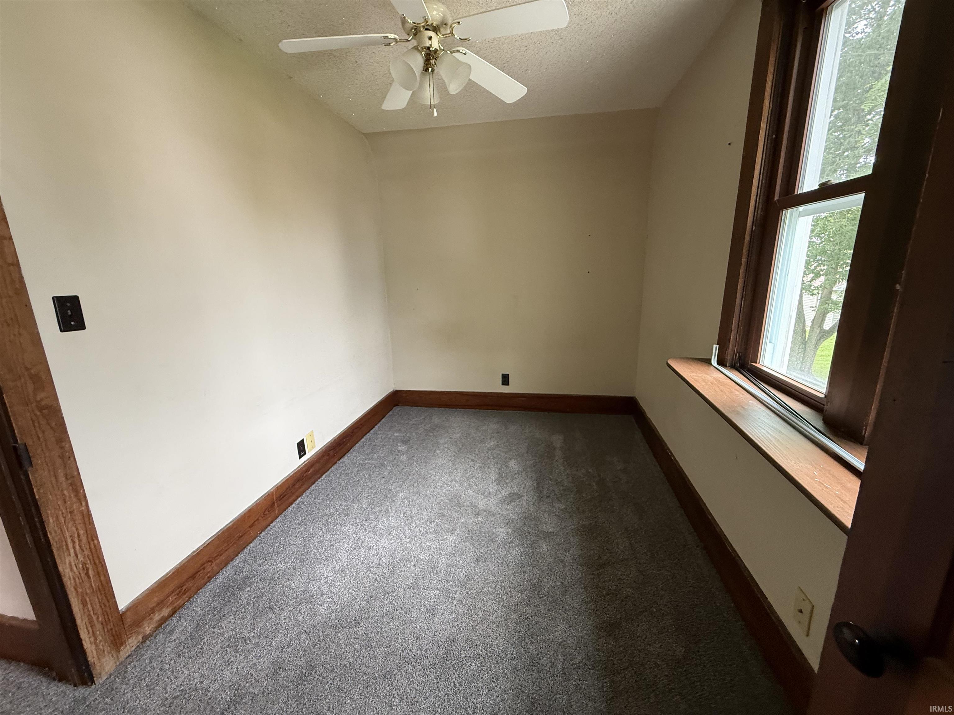 Carpeted room featuring a ceiling fan, a window with wood trim, and wood baseboards