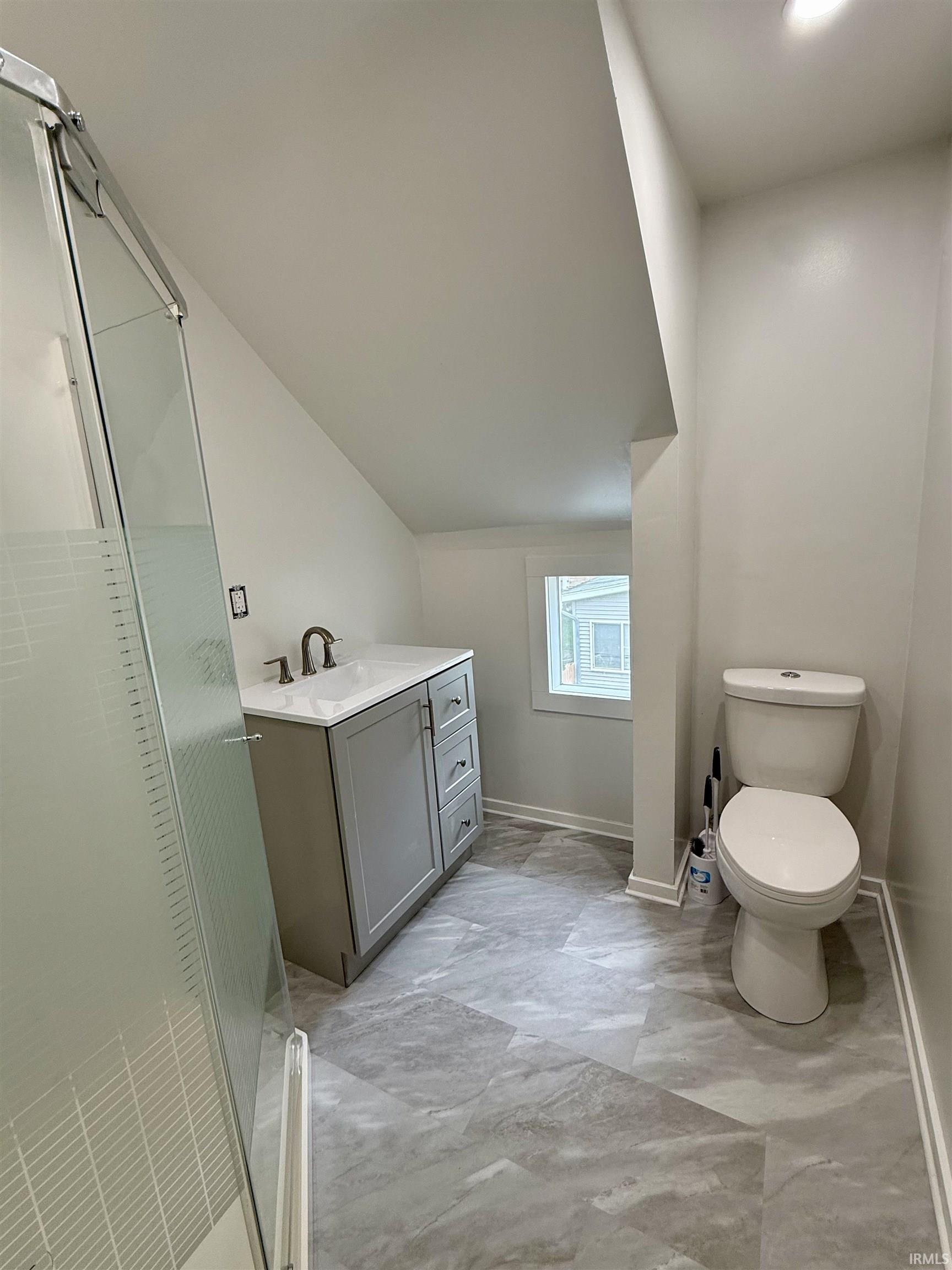 Contemporary bathroom featuring a glass-enclosed shower with textured privacy panel, a sleek gray vanity with integrated sink, modern chrome faucet, and geometric-patterned floor tiles