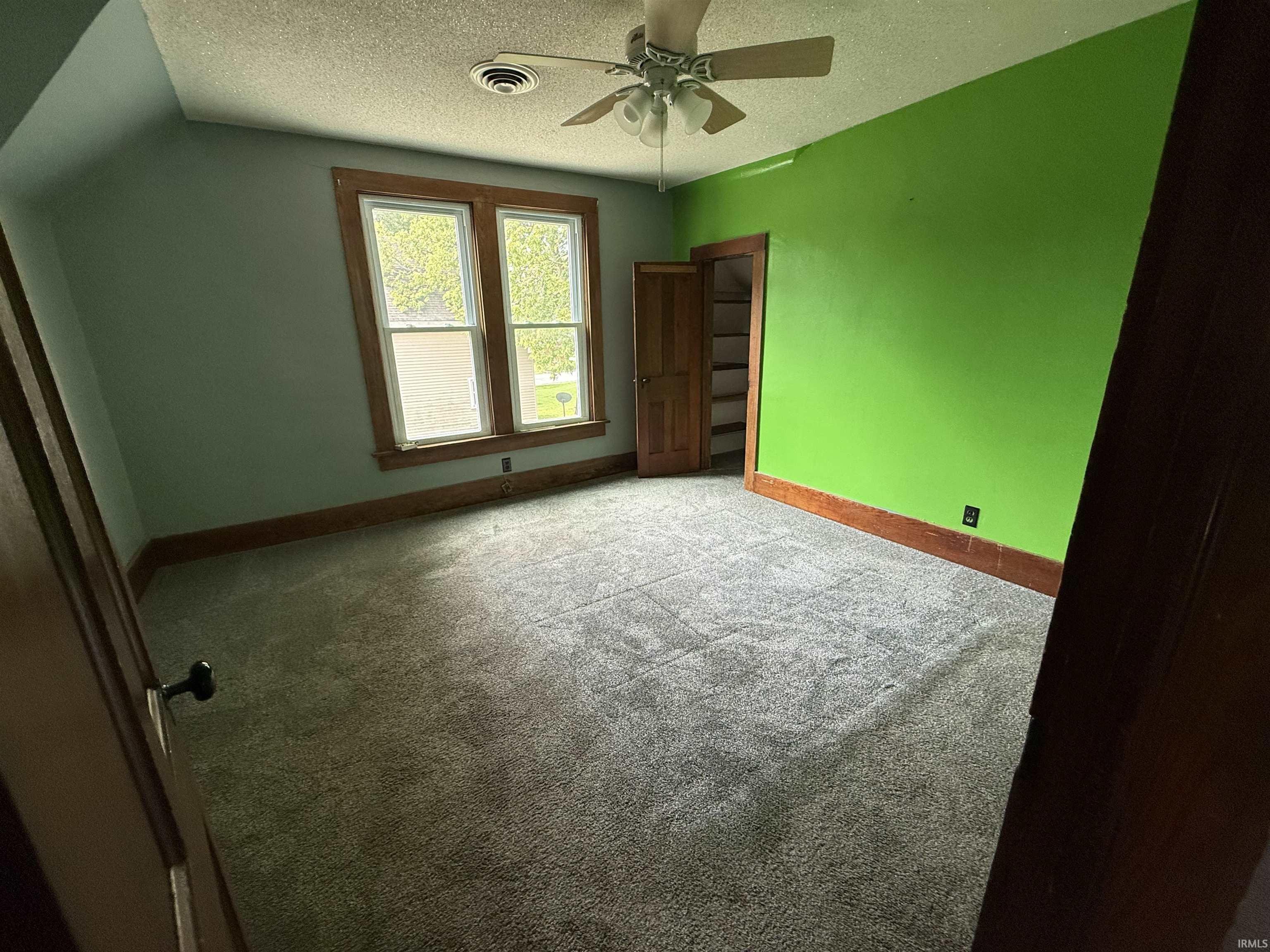 Spacious room featuring light gray carpeting, a ceiling fan, and a double window with wood trim