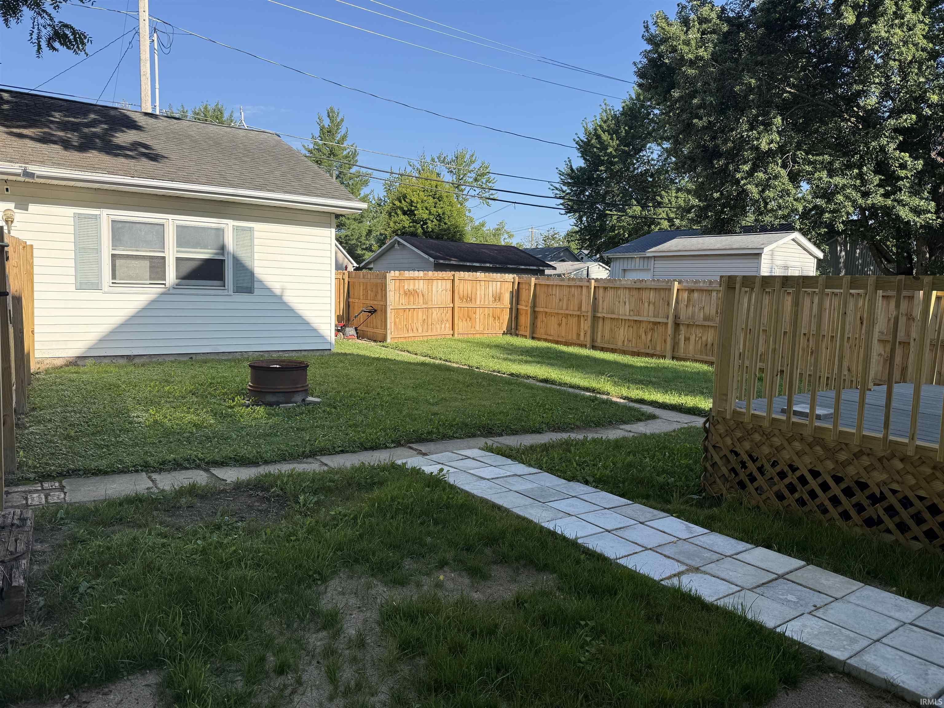 Enclosed backyard featuring a privacy fence, stone paver pathway, and a built-in fire pit