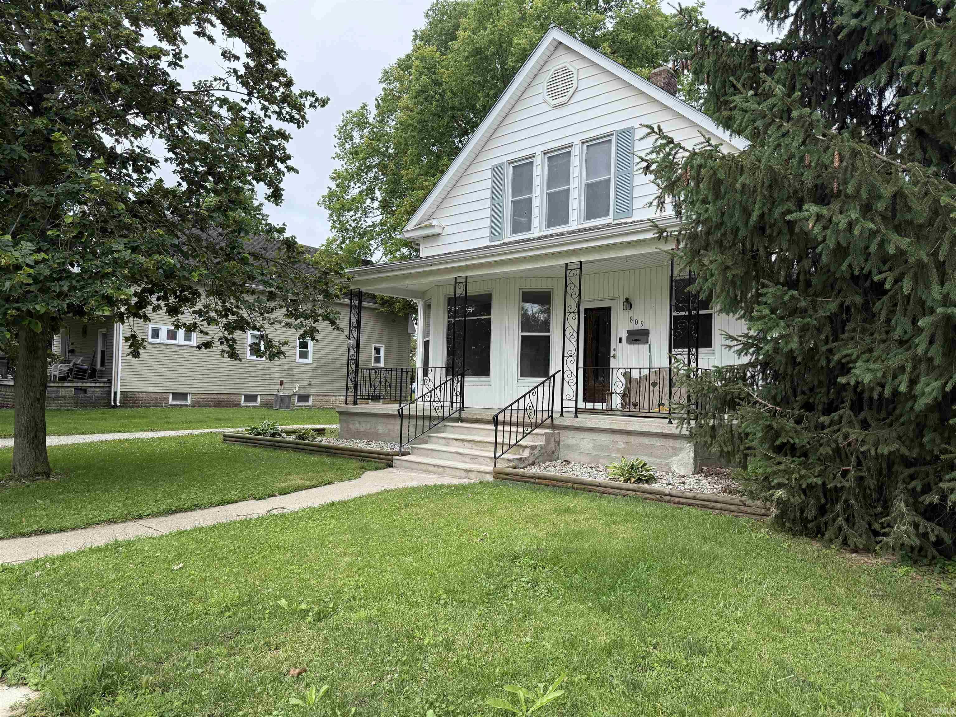 Gable-front home featuring white siding and a covered front porch with decorative black ironwork