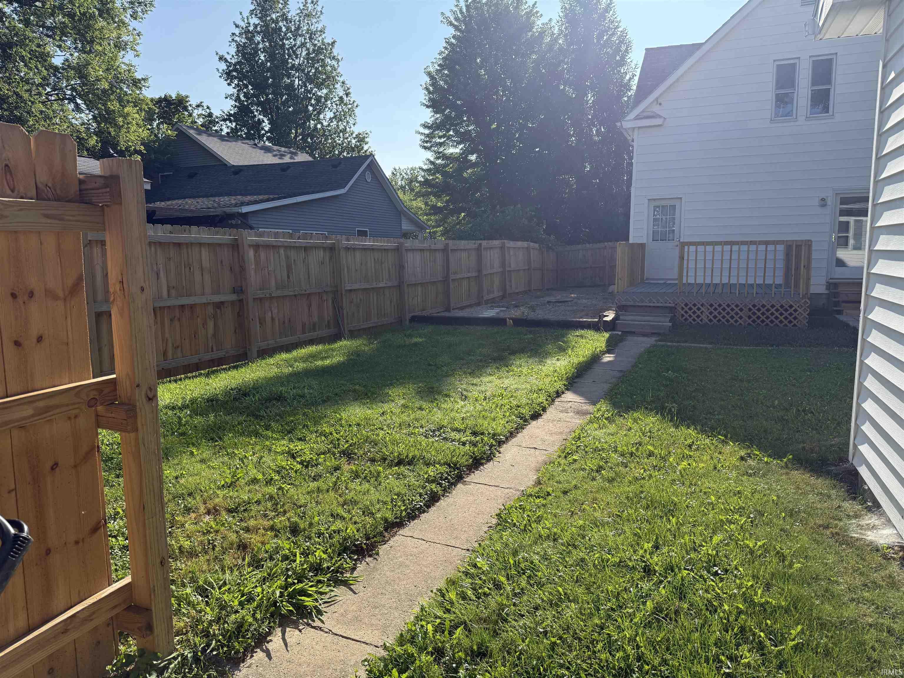 Expansive backyard featuring a new wood privacy fence, concrete pathway, and a wood deck