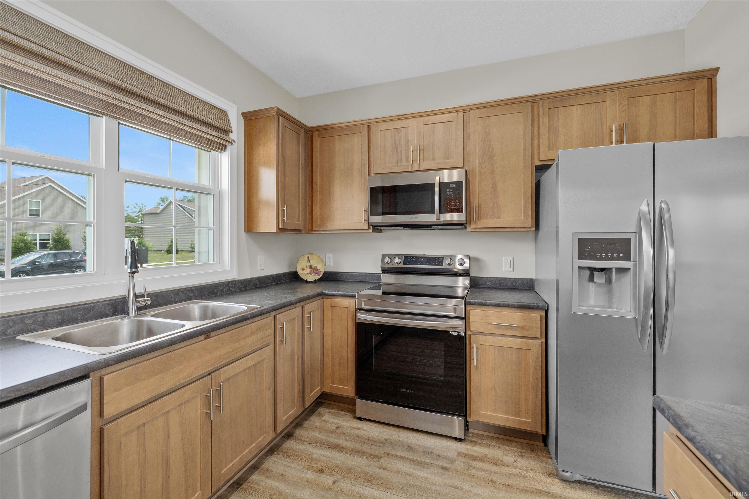 Modern kitchen featuring light wood cabinetry, stainless steel appliances, dark countertops, and wood-finish flooring