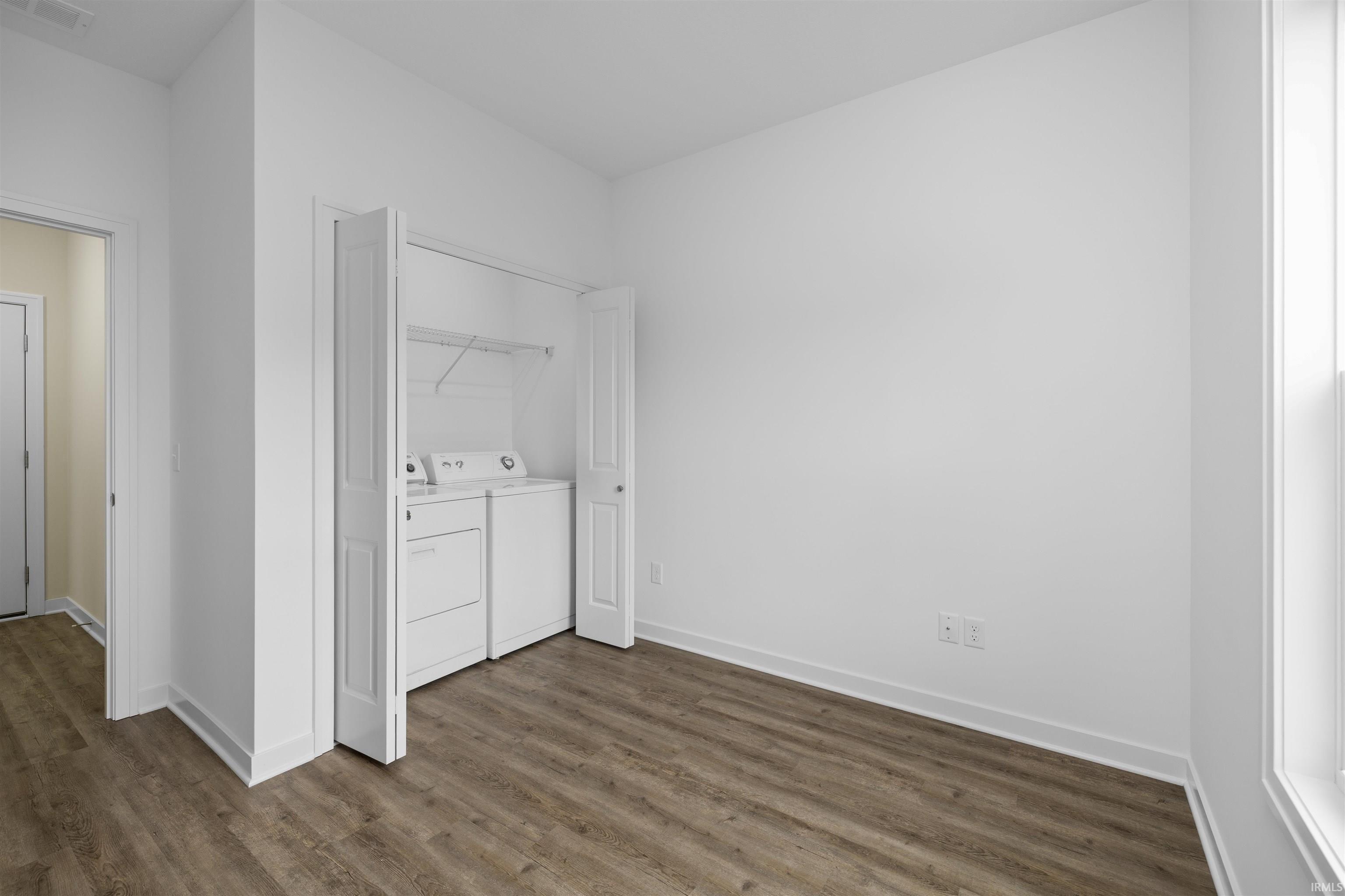 In-unit laundry closet with bifold doors, wood-finish flooring, white baseboards, and a window with white trim
