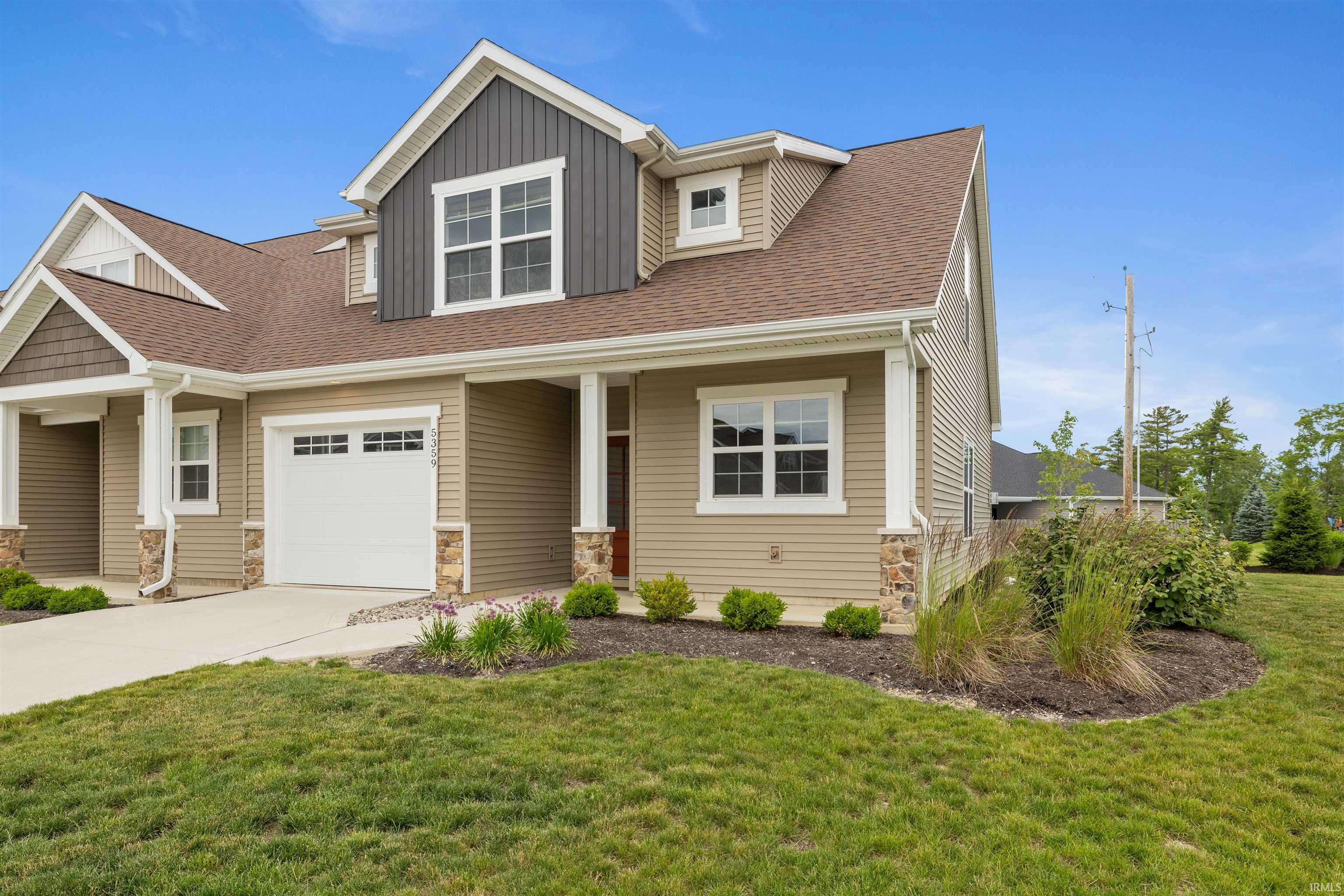 Contemporary multi-story exterior featuring tan siding, a combination of board and batten and horizontal paneling, a brown shingle roof, white trim windows, and a paved driveway leading to an integrated garage