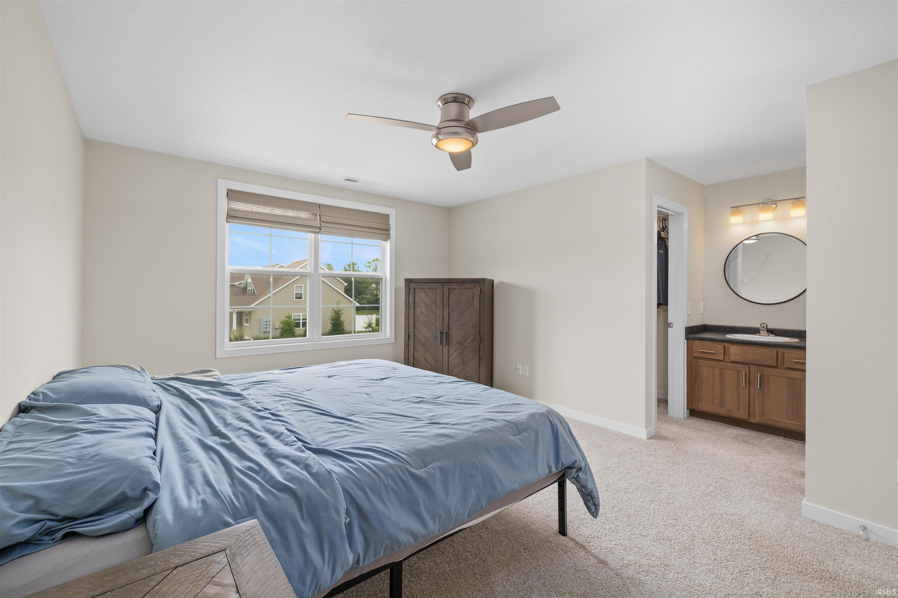 Carpeted room with a ceiling fan, a double window with blinds, and a vanity featuring a single sink, dark countertop, and an oval mirror