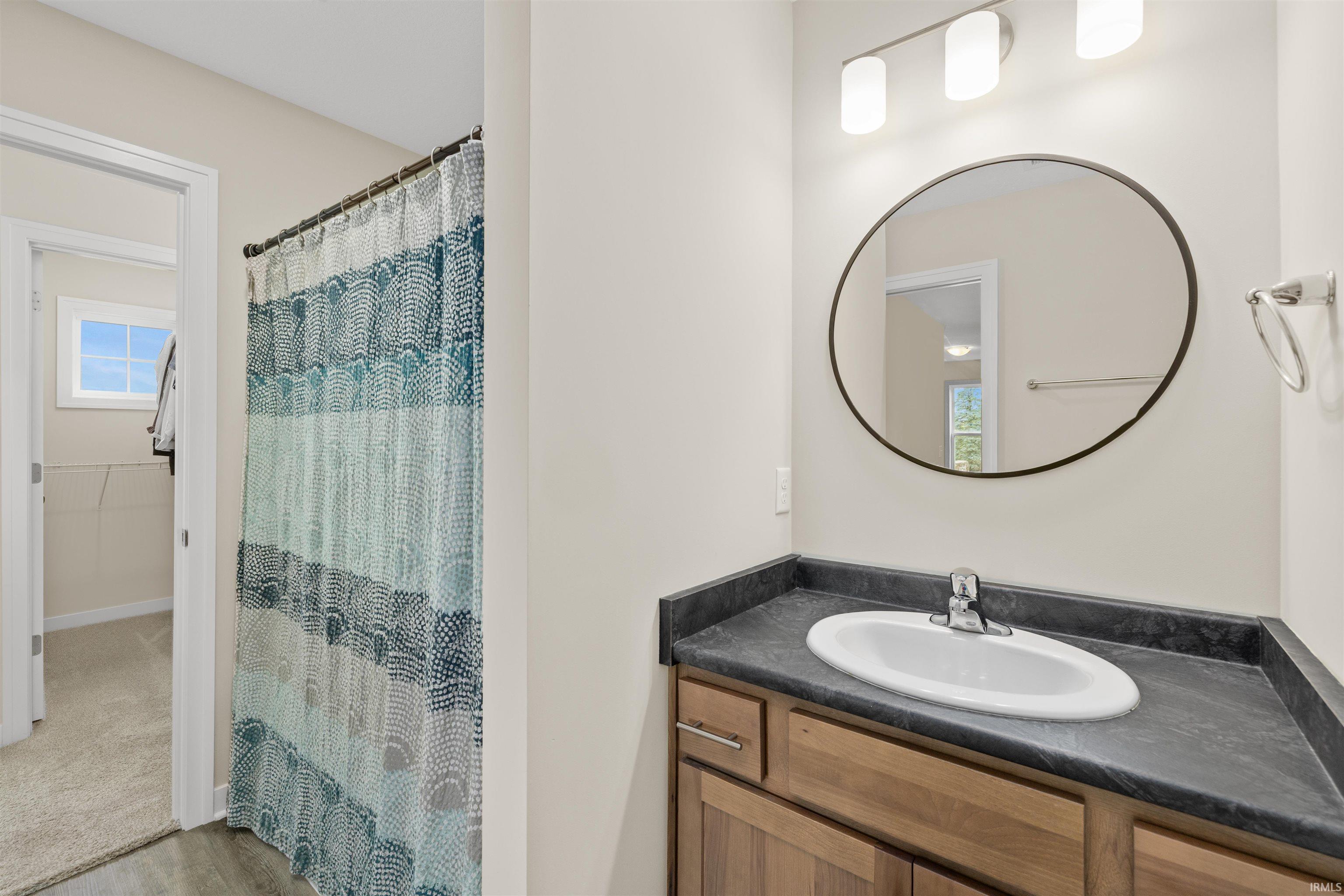 Vanity with a laminate countertop and integrated sink, complemented by a round framed mirror and a three-light fixture
