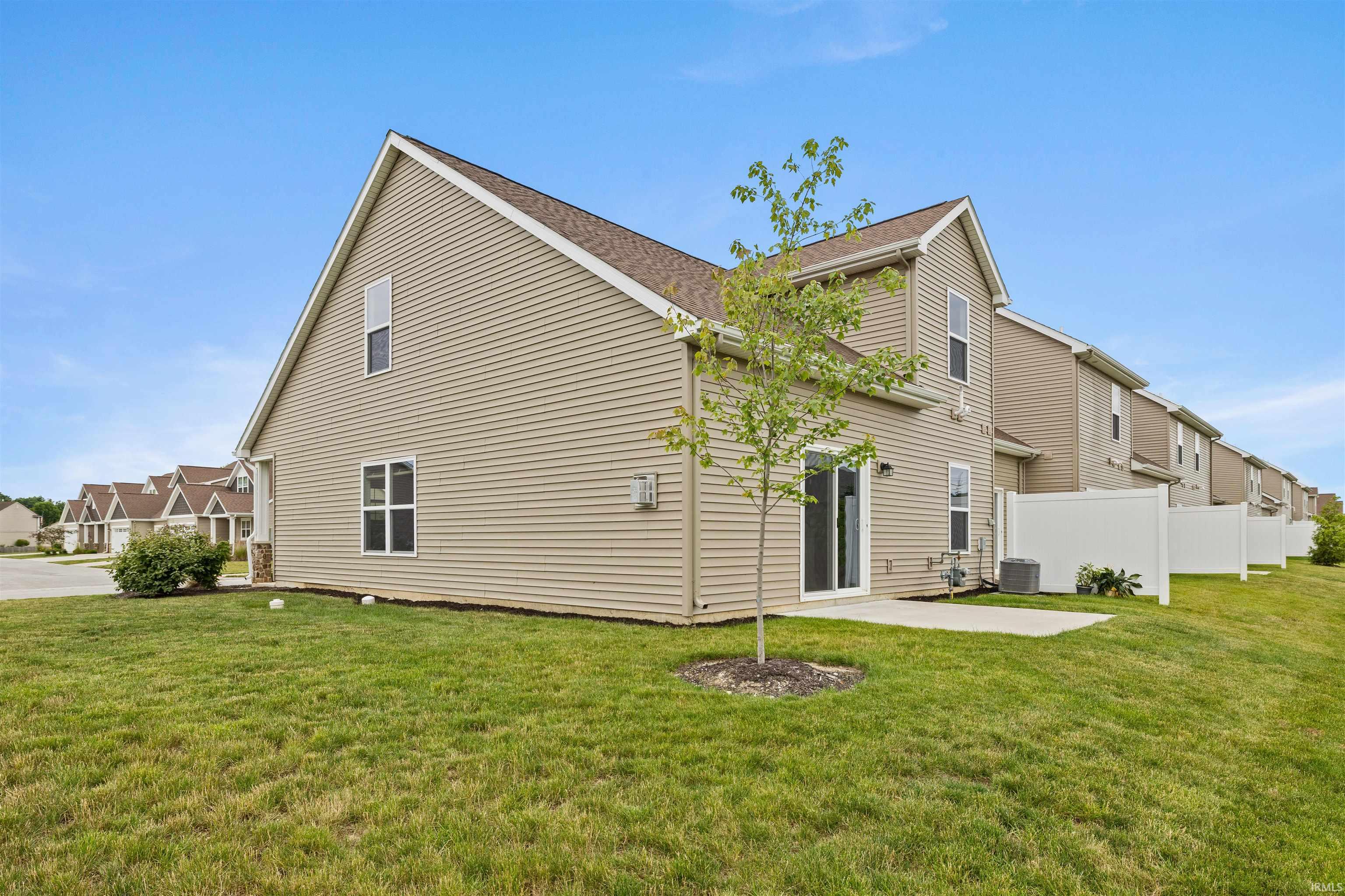 Rear exterior featuring tan siding, a gabled roofline, and a sliding glass door providing patio access
