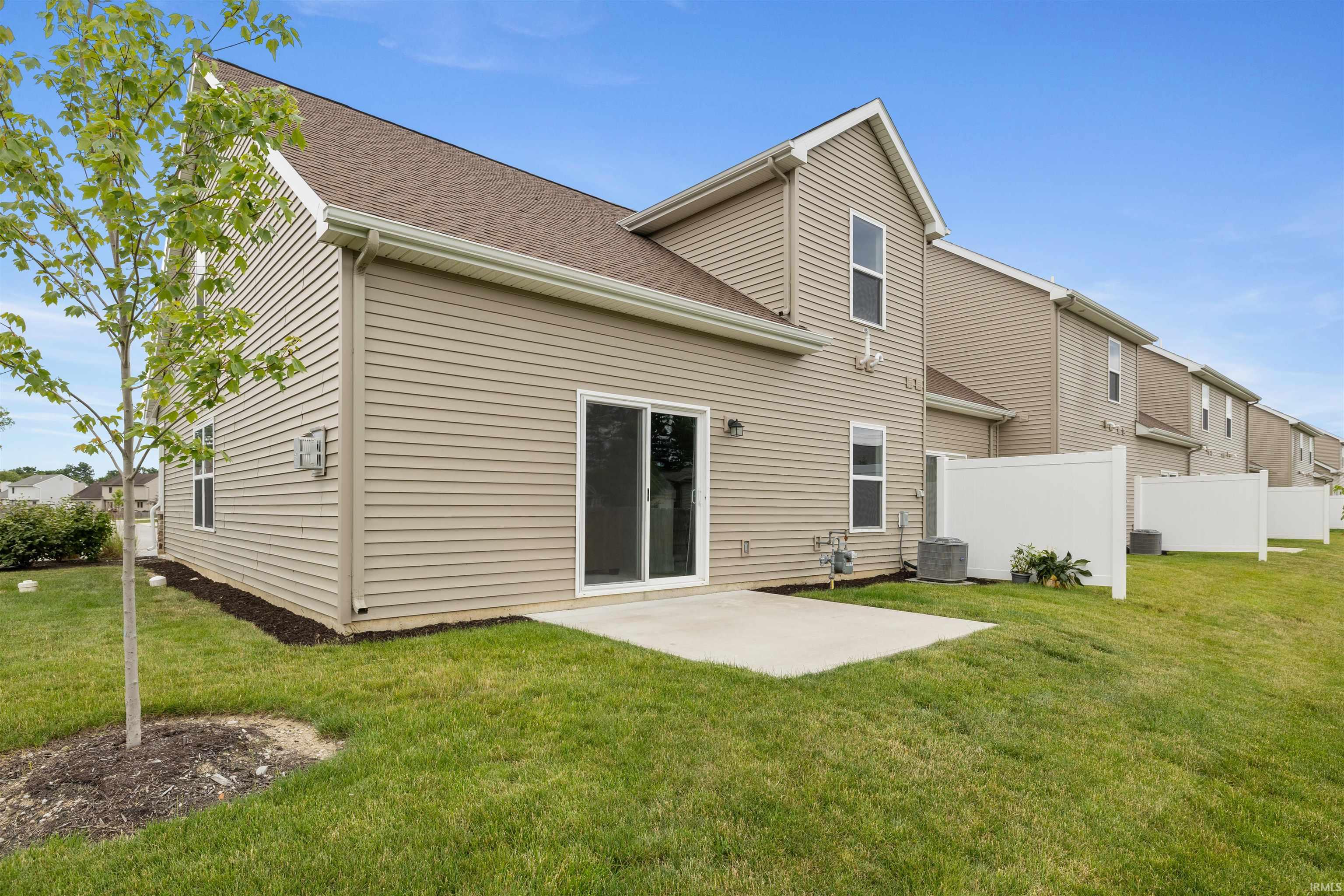 Rear exterior featuring a sliding glass door, concrete patio, tan siding, and a gabled roofline