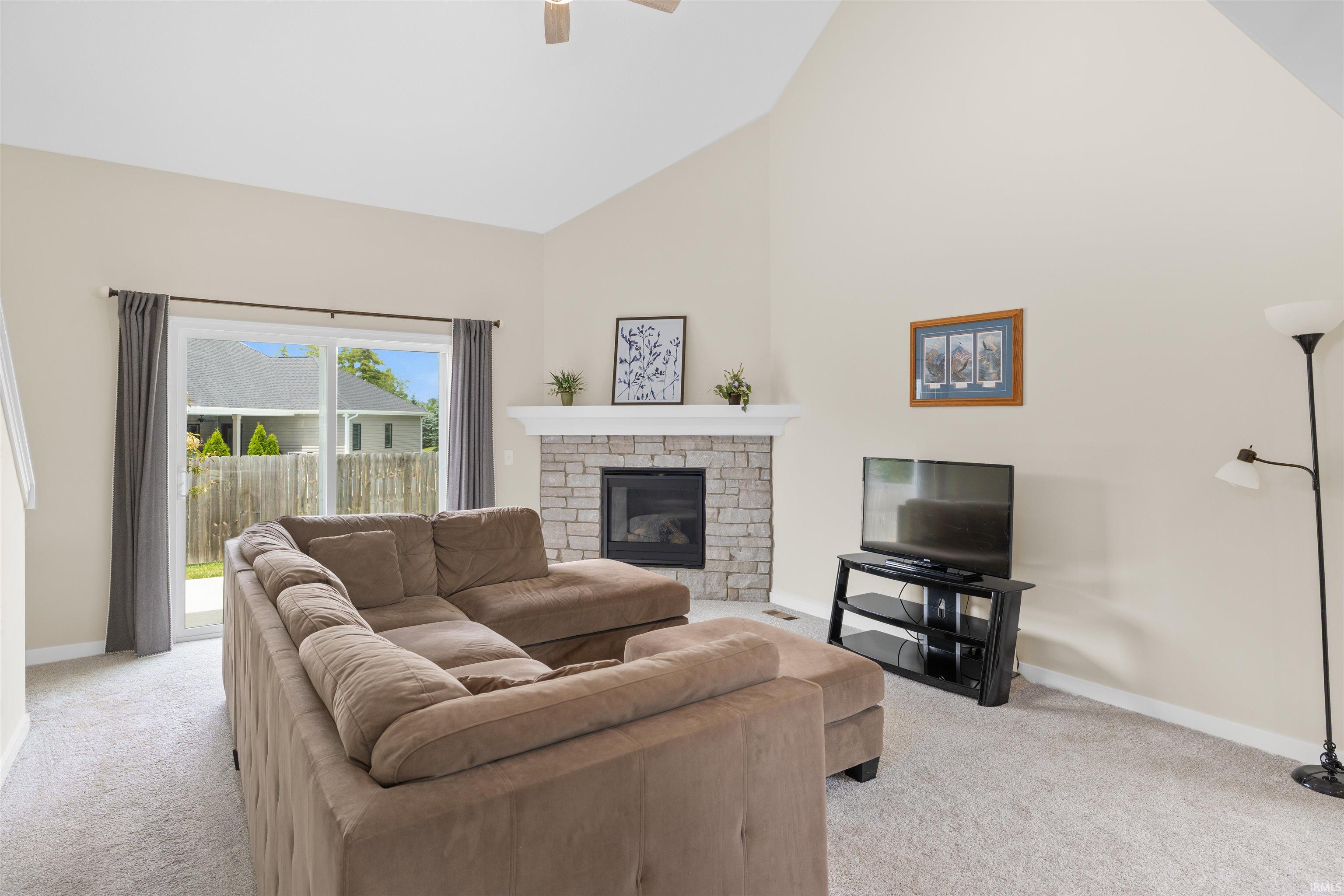 Spacious living area featuring a stone-clad fireplace with a white mantel, vaulted ceiling, and sliding glass doors