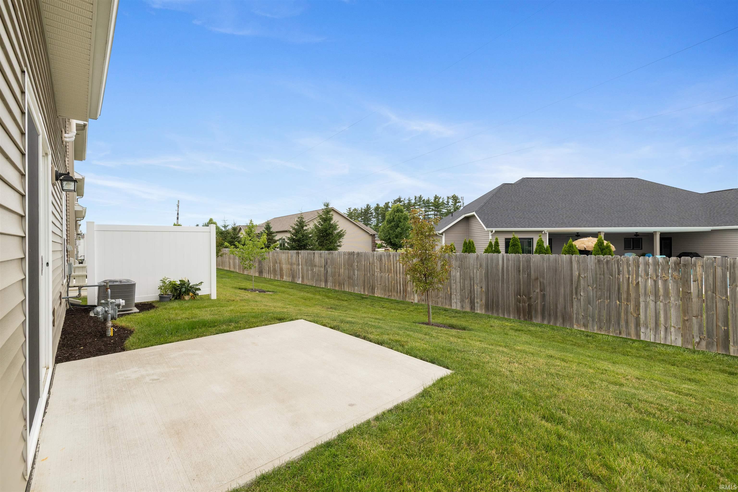 Expansive backyard featuring a concrete patio, verdant lawn, wooden privacy fencing, and a side access door