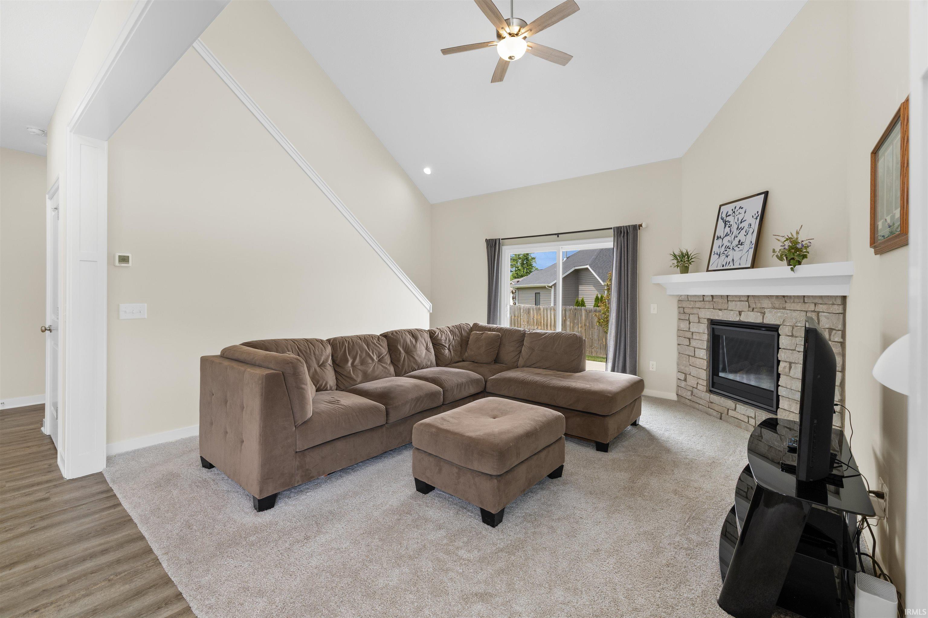 Vaulted ceiling living space featuring a stone-surround fireplace with a white mantel, sliding glass door access to the outdoors, and a ceiling fan with integrated lighting