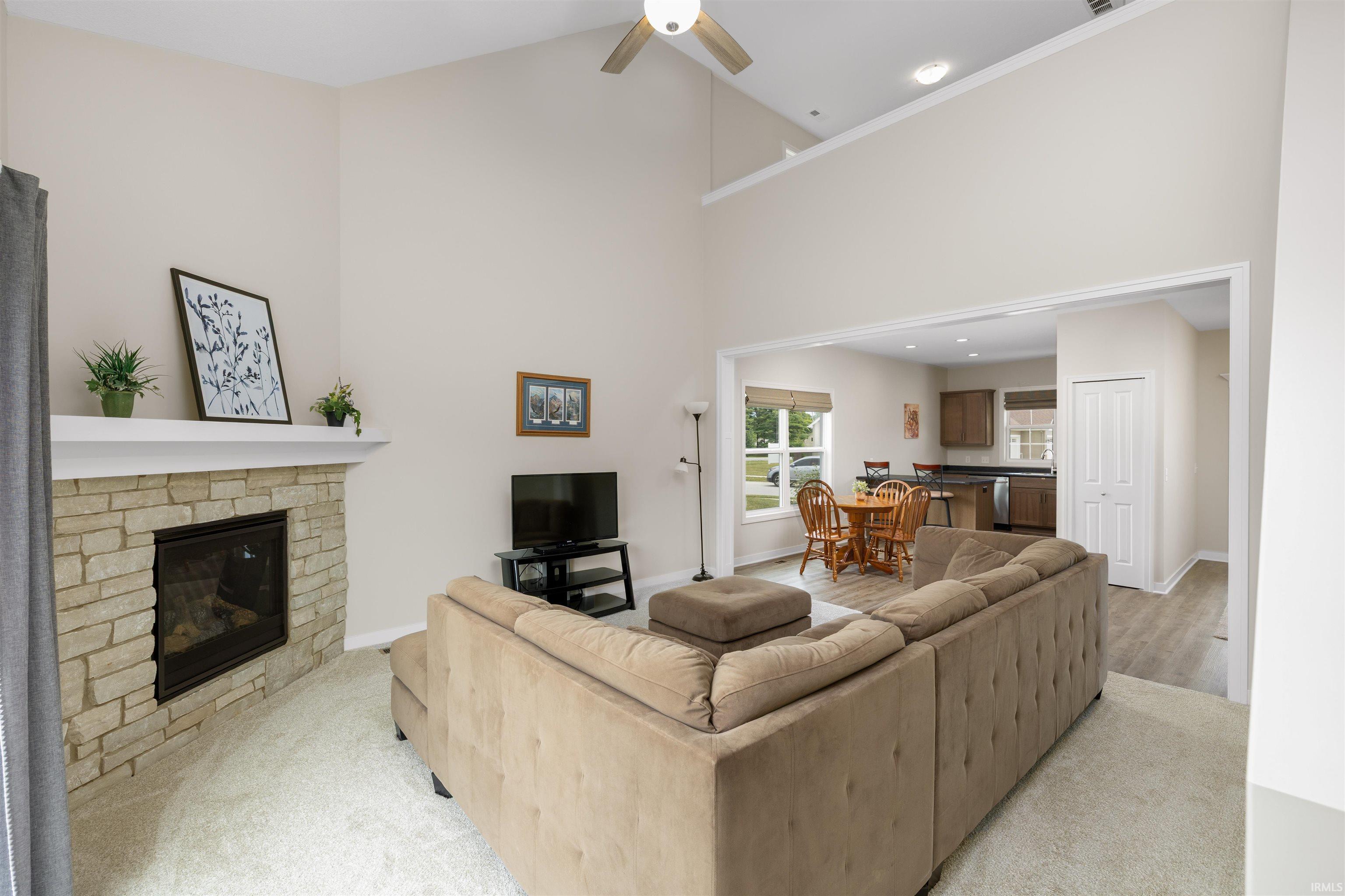 Living area featuring a stone fireplace with a white mantel, vaulted ceilings, and a ceiling fan