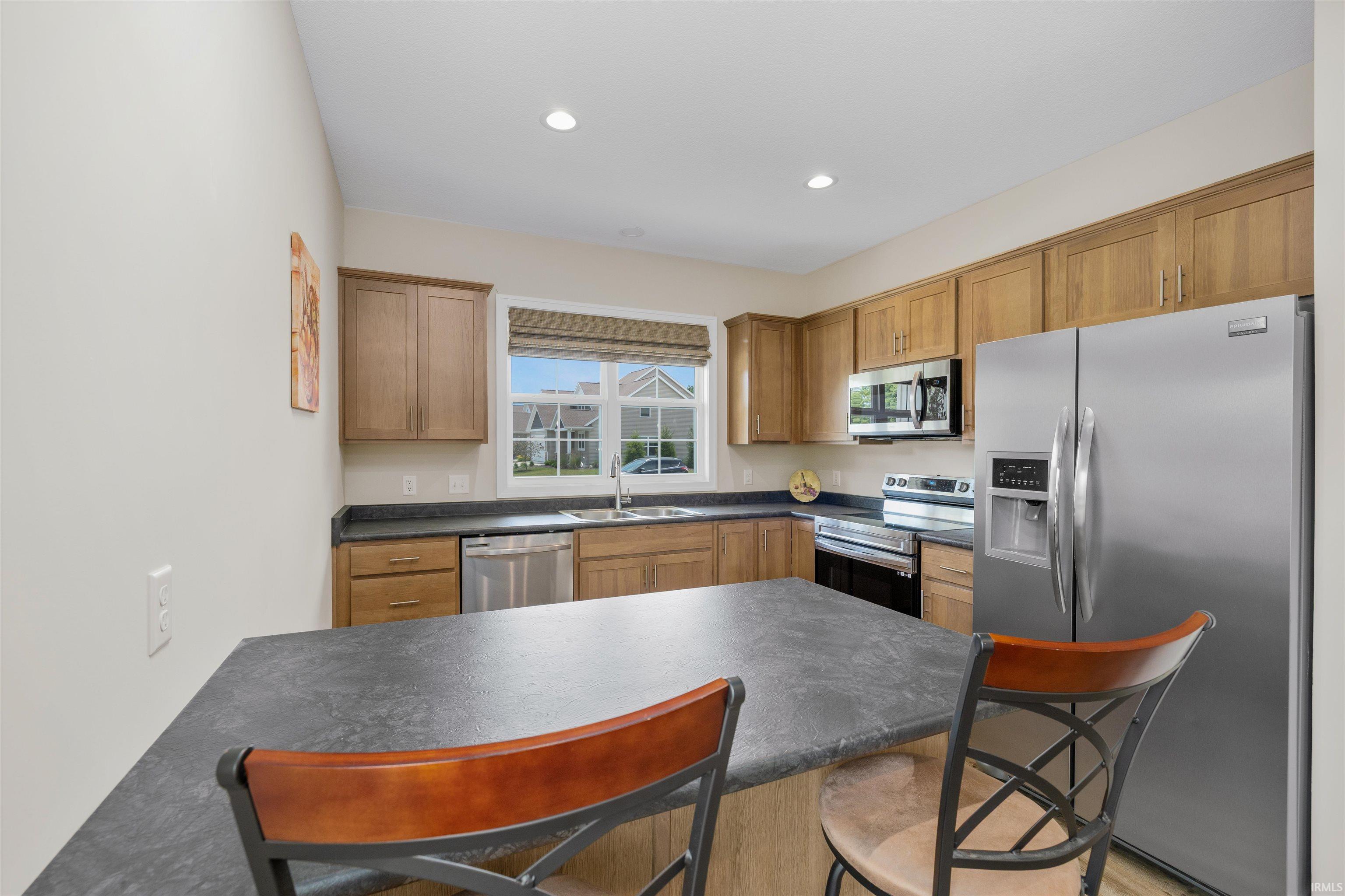 Kitchen featuring an island with a breakfast bar, stainless steel appliances, wood cabinetry, recessed lighting, and a double basin sink