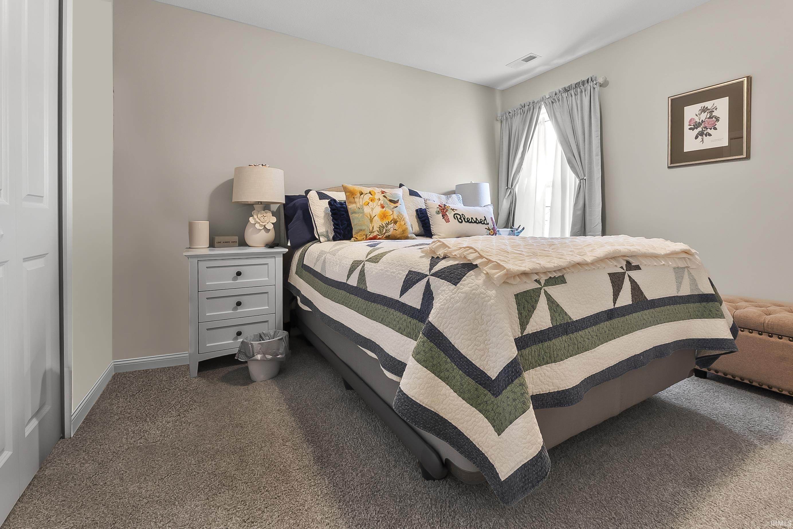 Carpeted bedroom featuring neutral wall paint, a window with curtains, and a white three-drawer nightstand