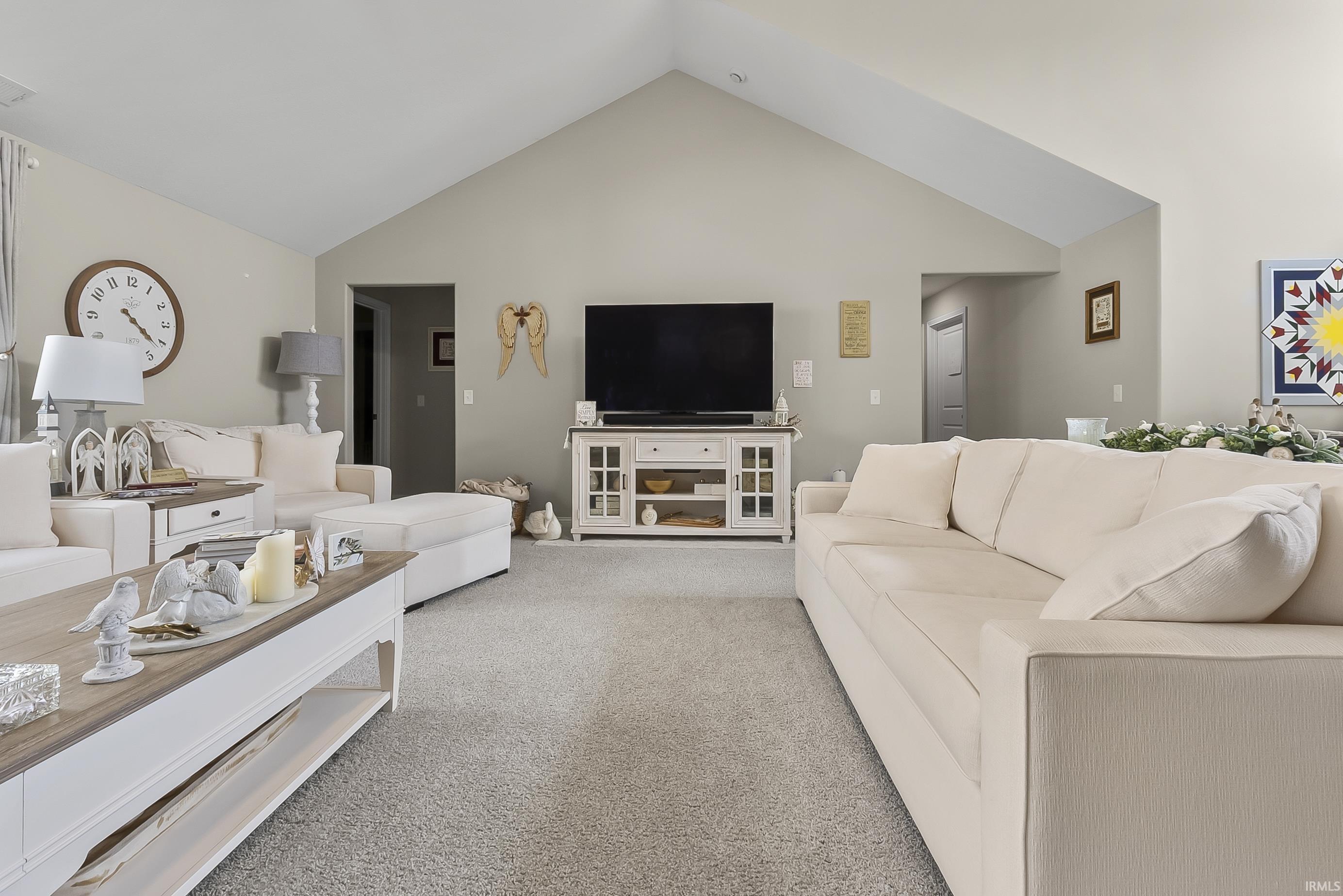 Spacious living area featuring a vaulted ceiling, neutral wall tones, and gray carpeting