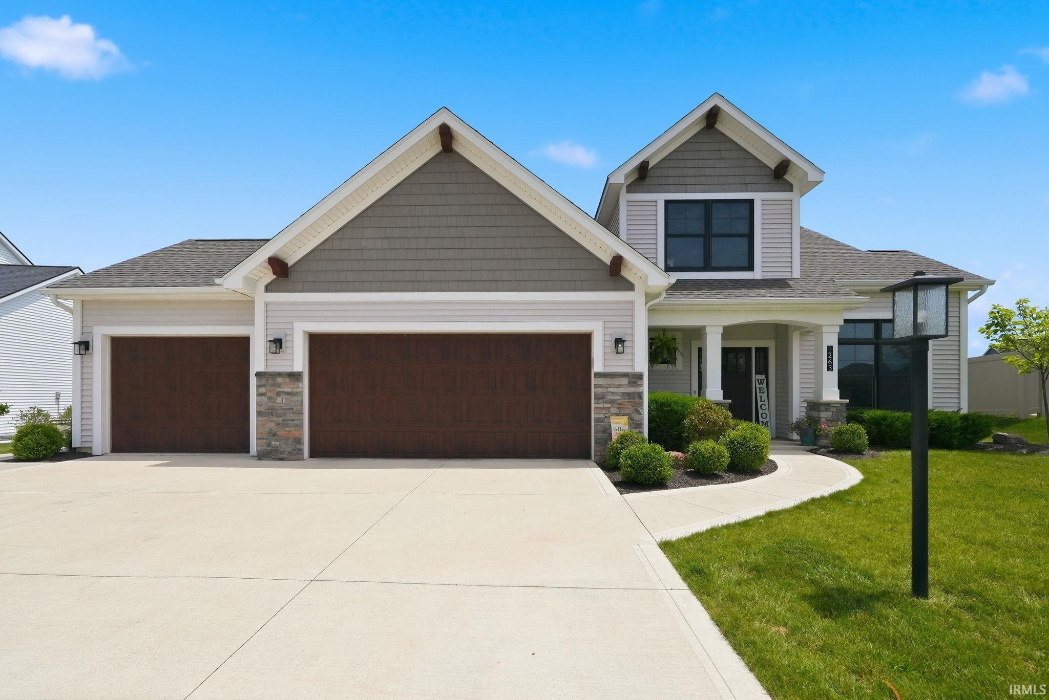 Contemporary residence featuring a two-car garage with dark wood-finish doors, a concrete driveway, a curved concrete walkway, and a covered entryway
