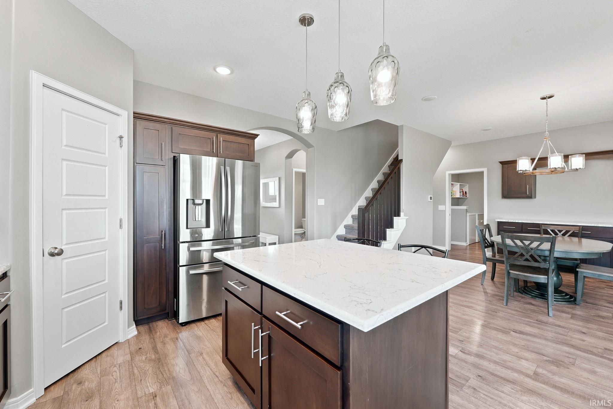 Kitchen featuring an island with a light-toned countertop, stainless steel refrigerator, dark wood-finish cabinetry, and wood-finish flooring