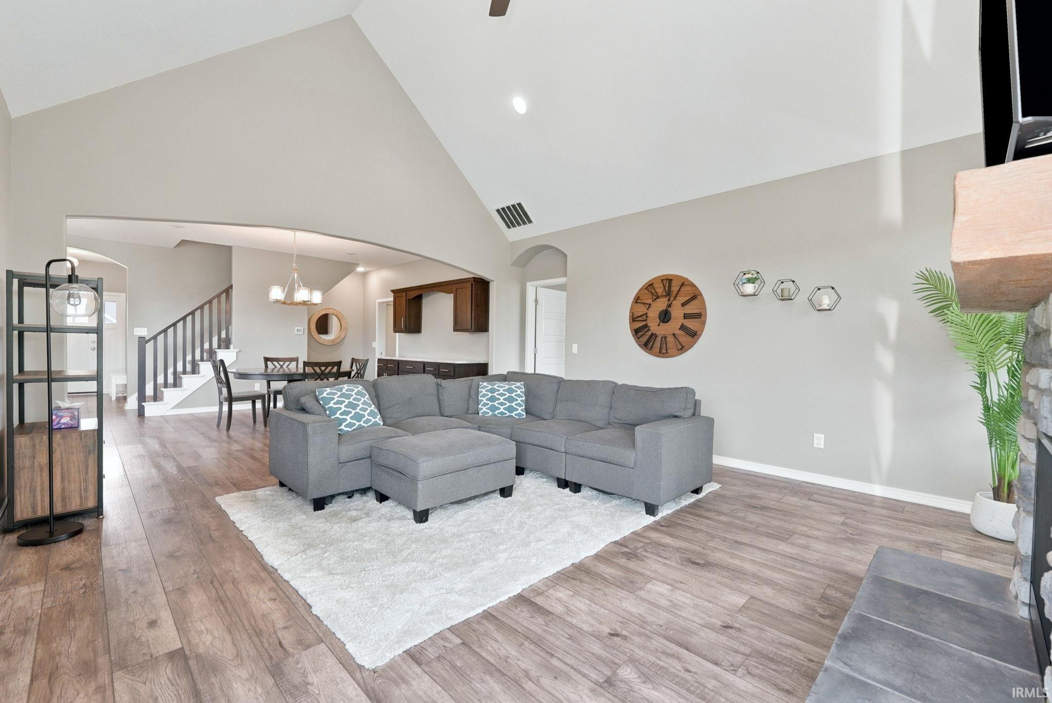 Vaulted ceiling living area featuring wood-finish flooring, a stone fireplace, and an arched entryway to the dining area
