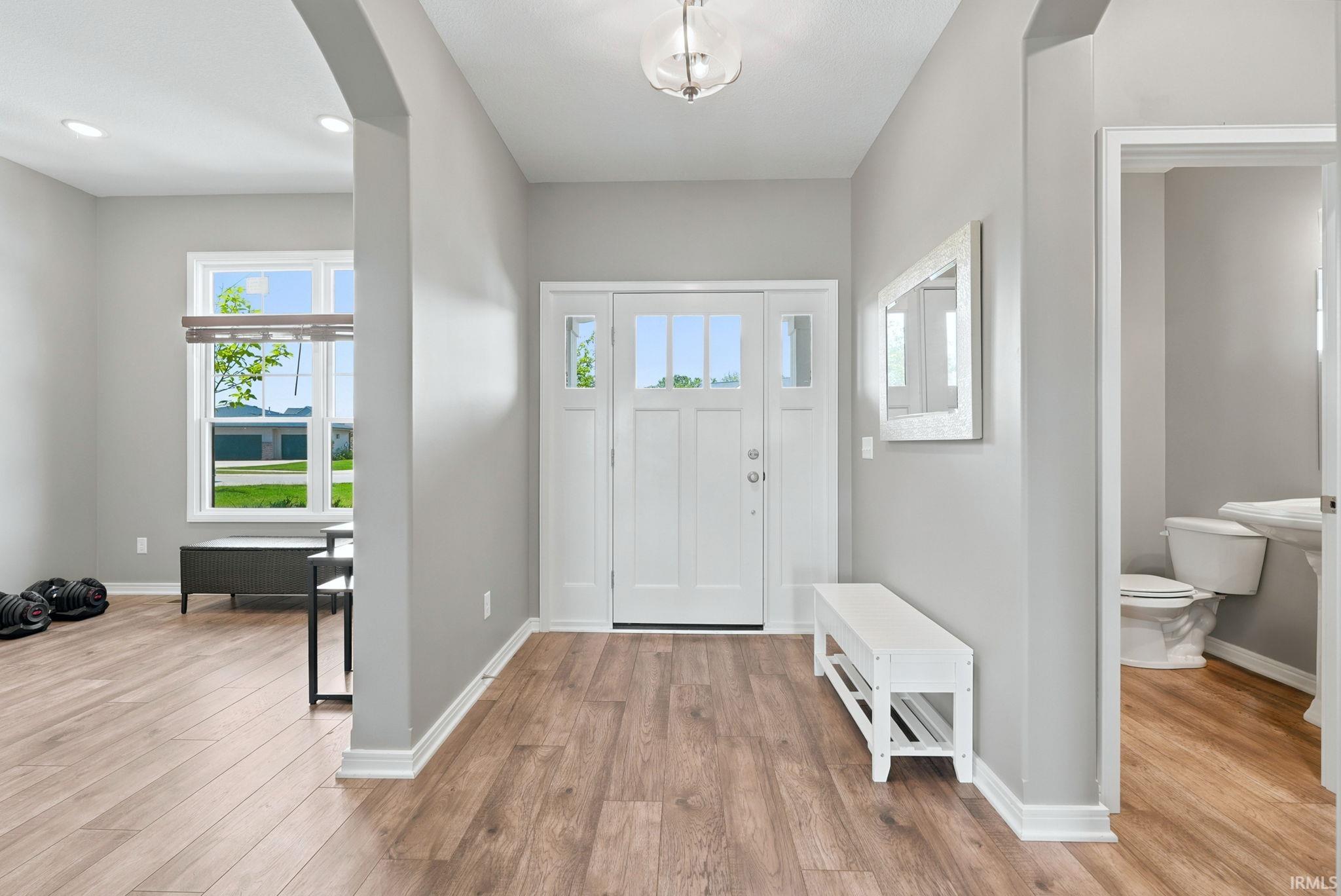 Bright entryway featuring wood-finish flooring, a contemporary overhead light fixture, and a white paneled front door with sidelights