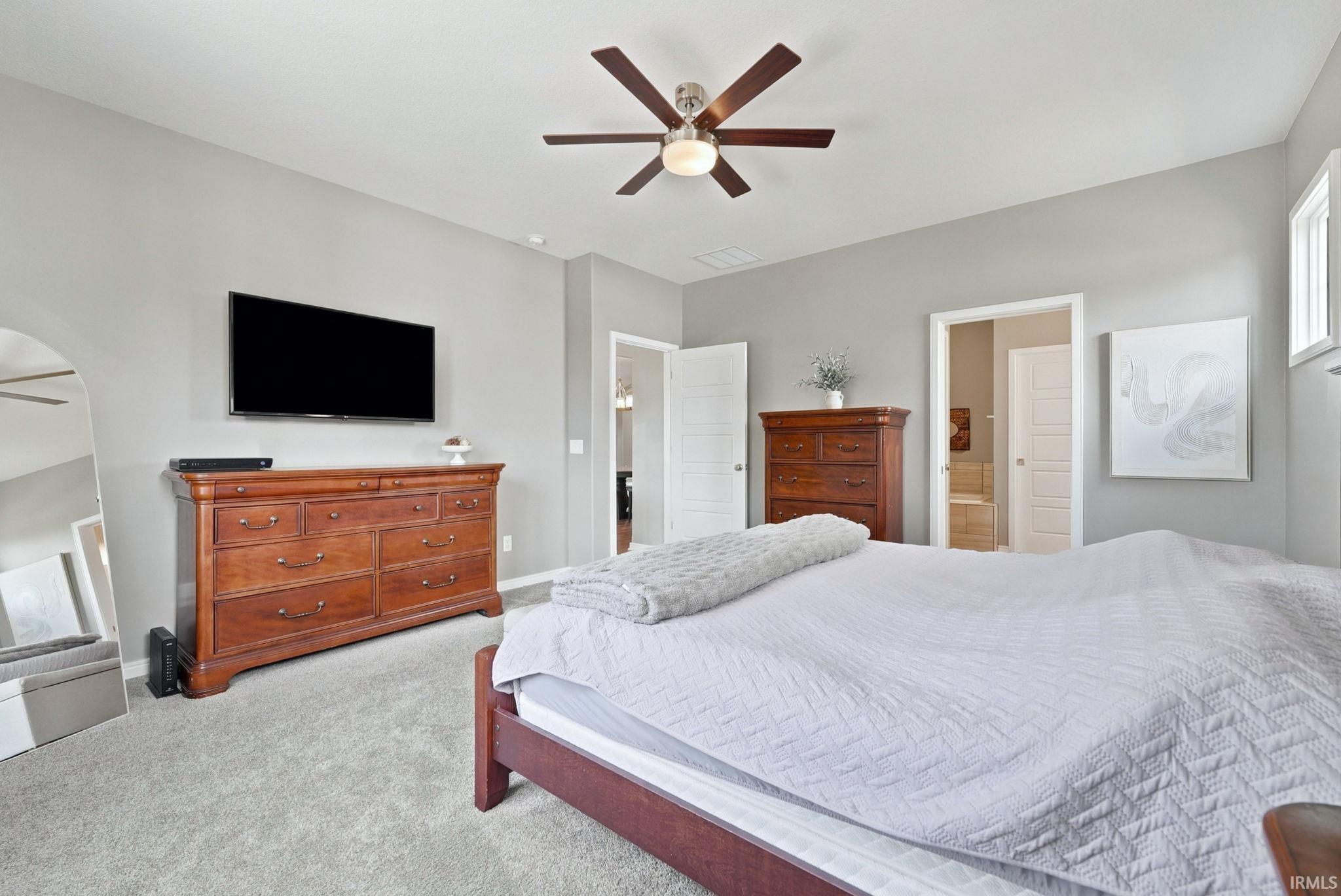 Spacious room featuring light gray walls, plush gray carpeting, and a ceiling fan with integrated lighting